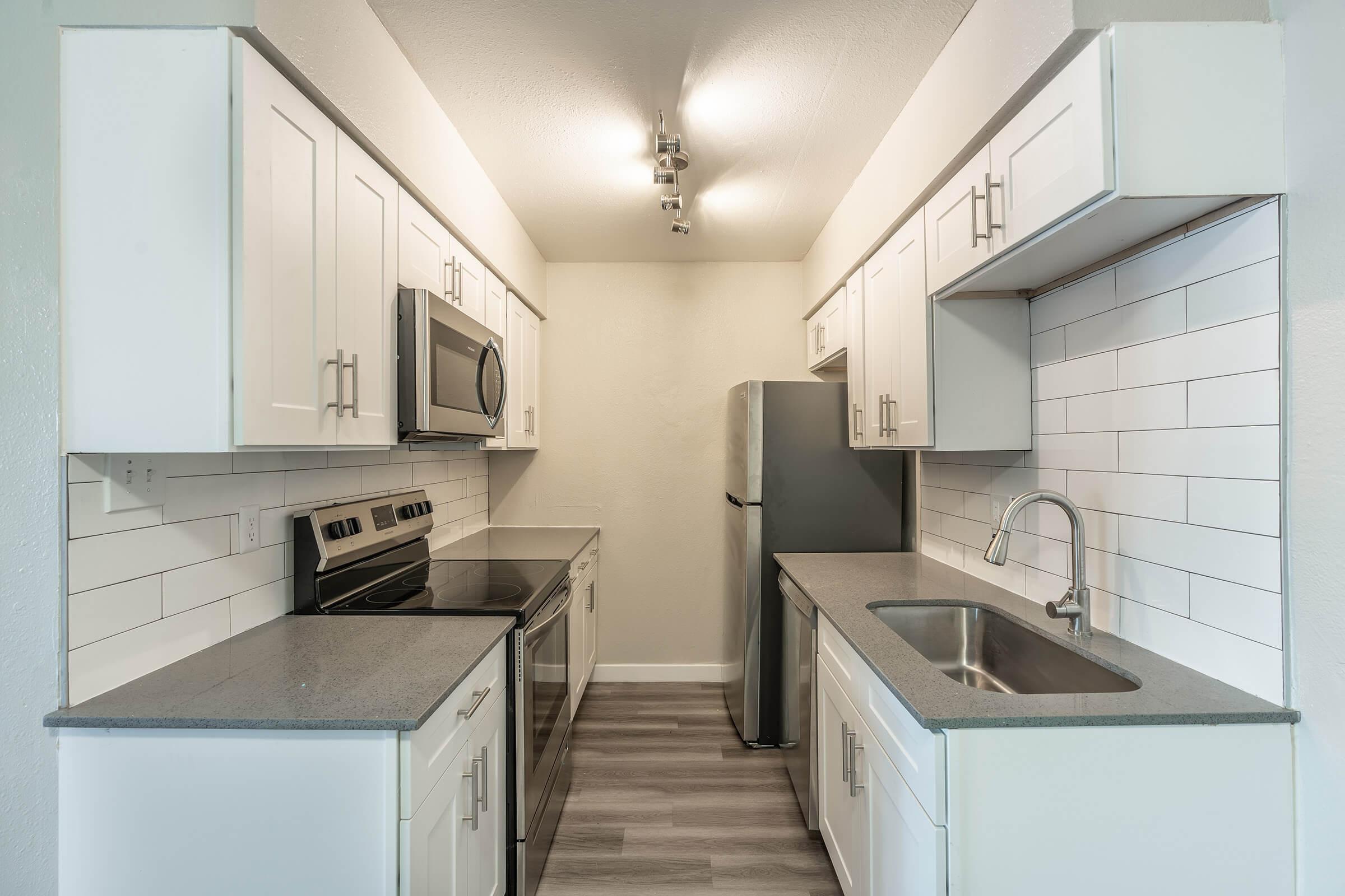 Galley way kitchen with white cabinets, white backsplash, and grey quartz counters