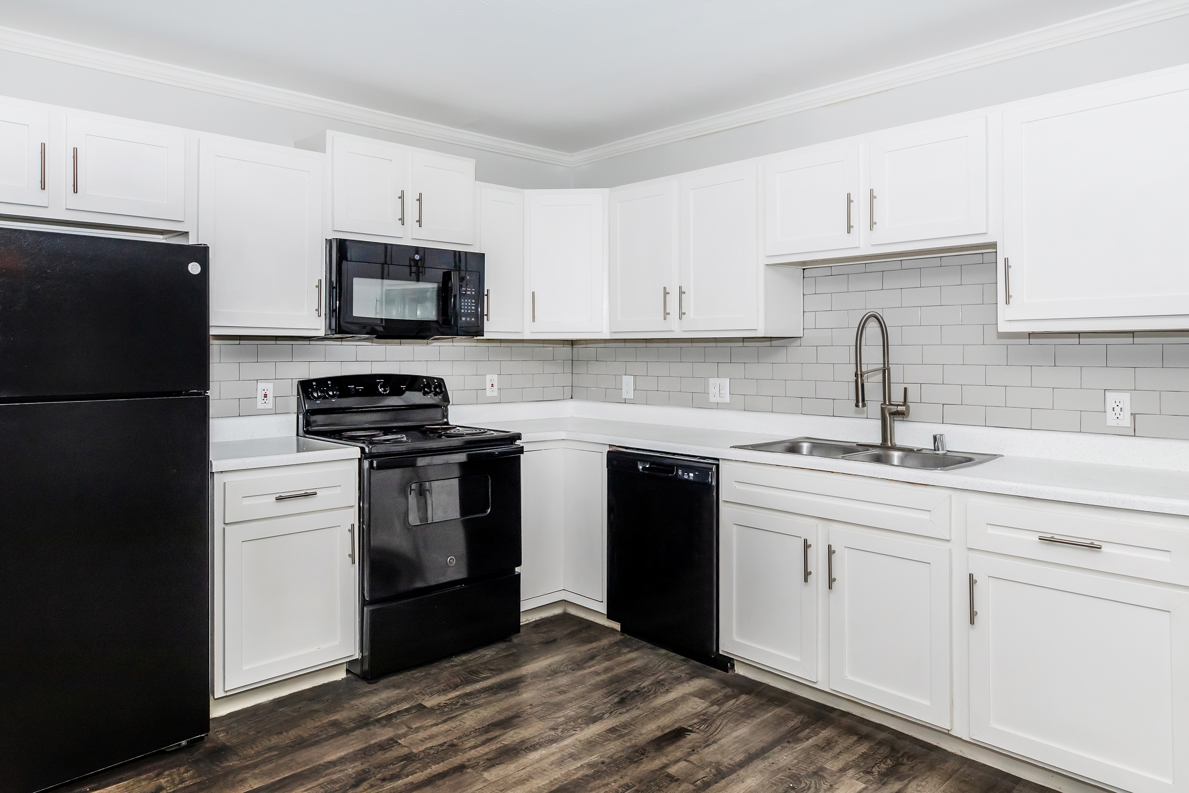 Modern kitchen featuring white cabinets, a black refrigerator, a black stove, a black microwave, and a black dishwasher. The countertops are light-colored with a tiled backsplash. The floor has a wood-like finish, enhancing the contemporary design of the space.
