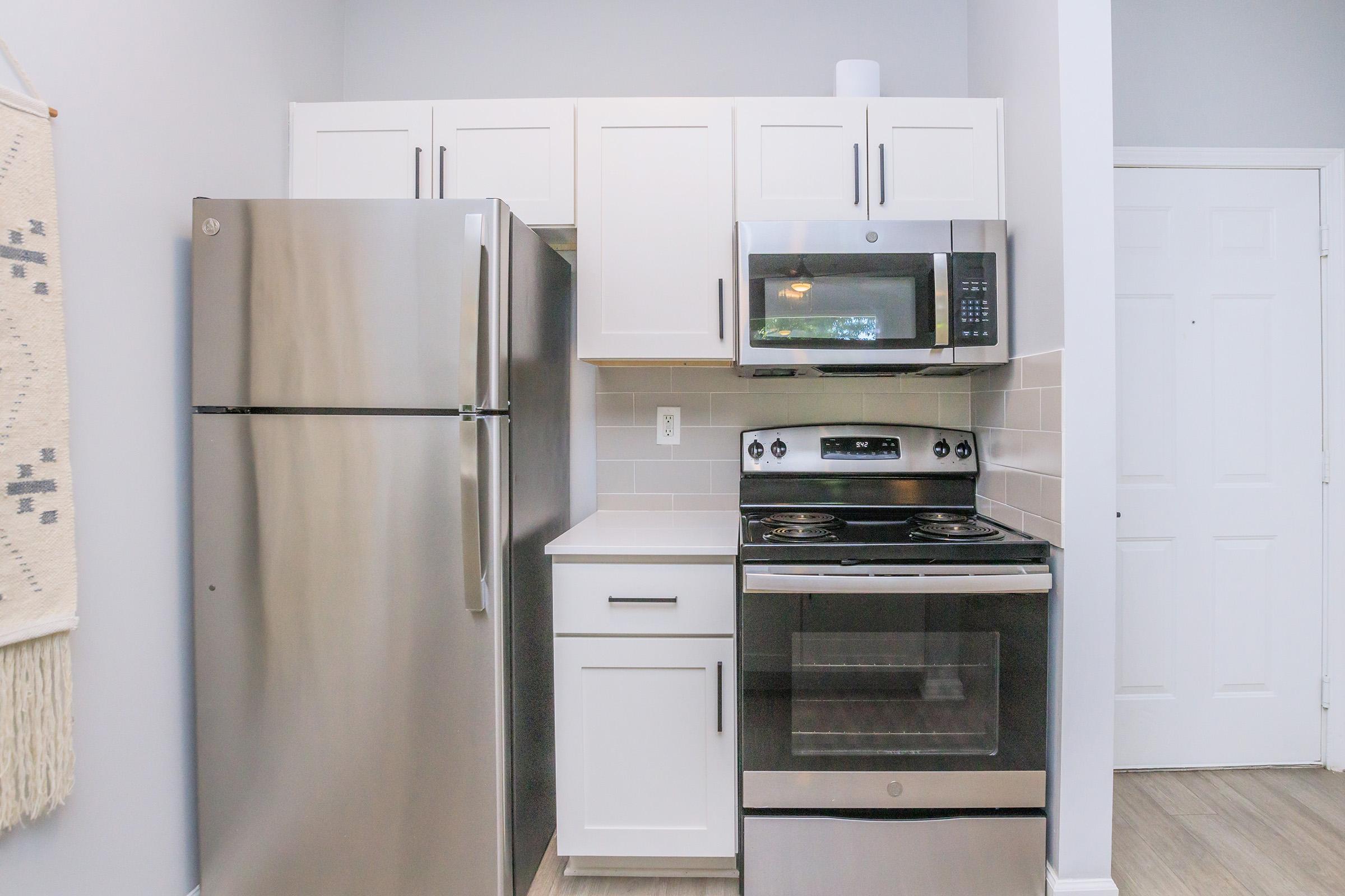 Modern kitchen featuring stainless steel appliances, including a refrigerator, microwave, and stove. The cabinetry is light-colored, and the countertops are sleek and minimalistic. Bright and airy atmosphere with a neutral color scheme, showcasing an organized and functional kitchen space.