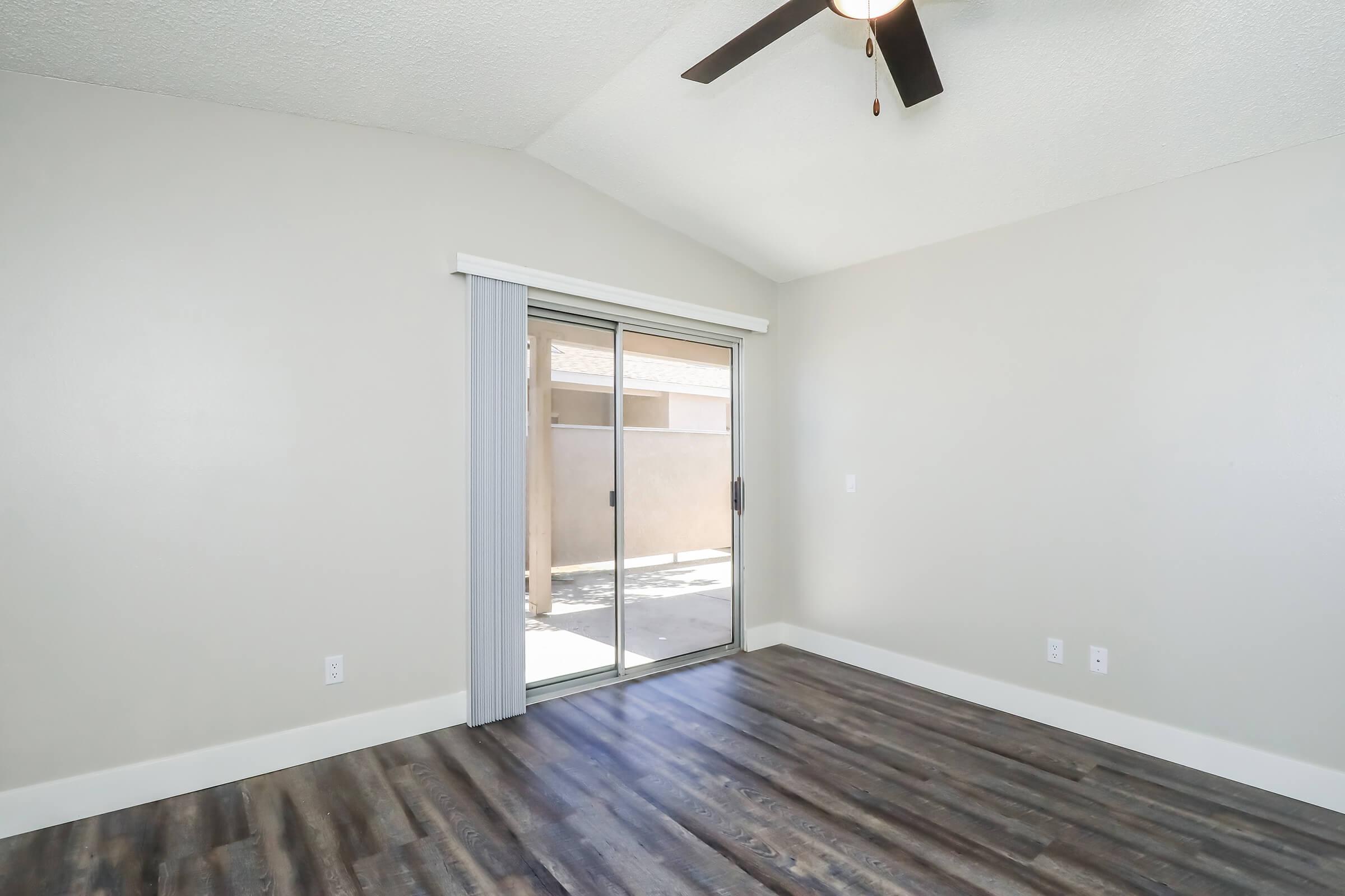 Spacious light-filled room featuring a ceiling fan, large sliding glass doors leading to a patio area, and modern laminate flooring. The walls are painted in a neutral color, enhancing the open and airy atmosphere. Ideal for a living room or personal retreat.