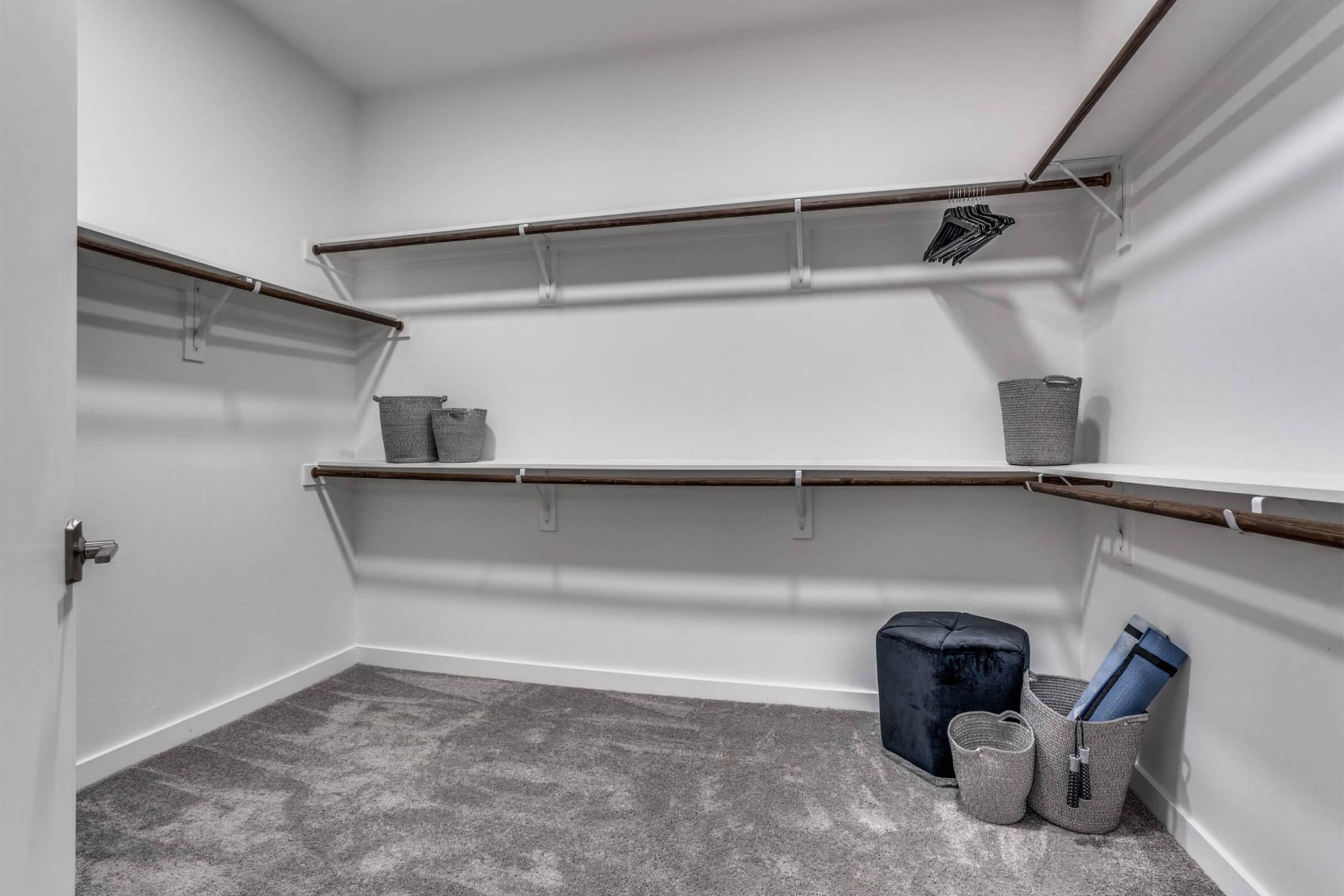 A spacious, empty closet featuring wooden shelves. There are a few storage baskets and a folded blanket on the floor. The walls are light-colored, and the carpet is plush, creating a clean and organized storage space.