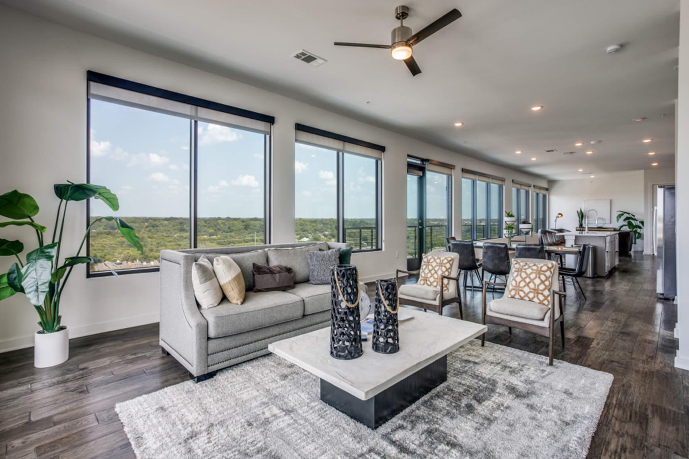 Spacious modern living room featuring a light gray sofa, decorative vases on a coffee table, and large windows offering a scenic view. The room is elegantly furnished with stylish chairs and a plush rug, contributing to a bright and airy atmosphere.