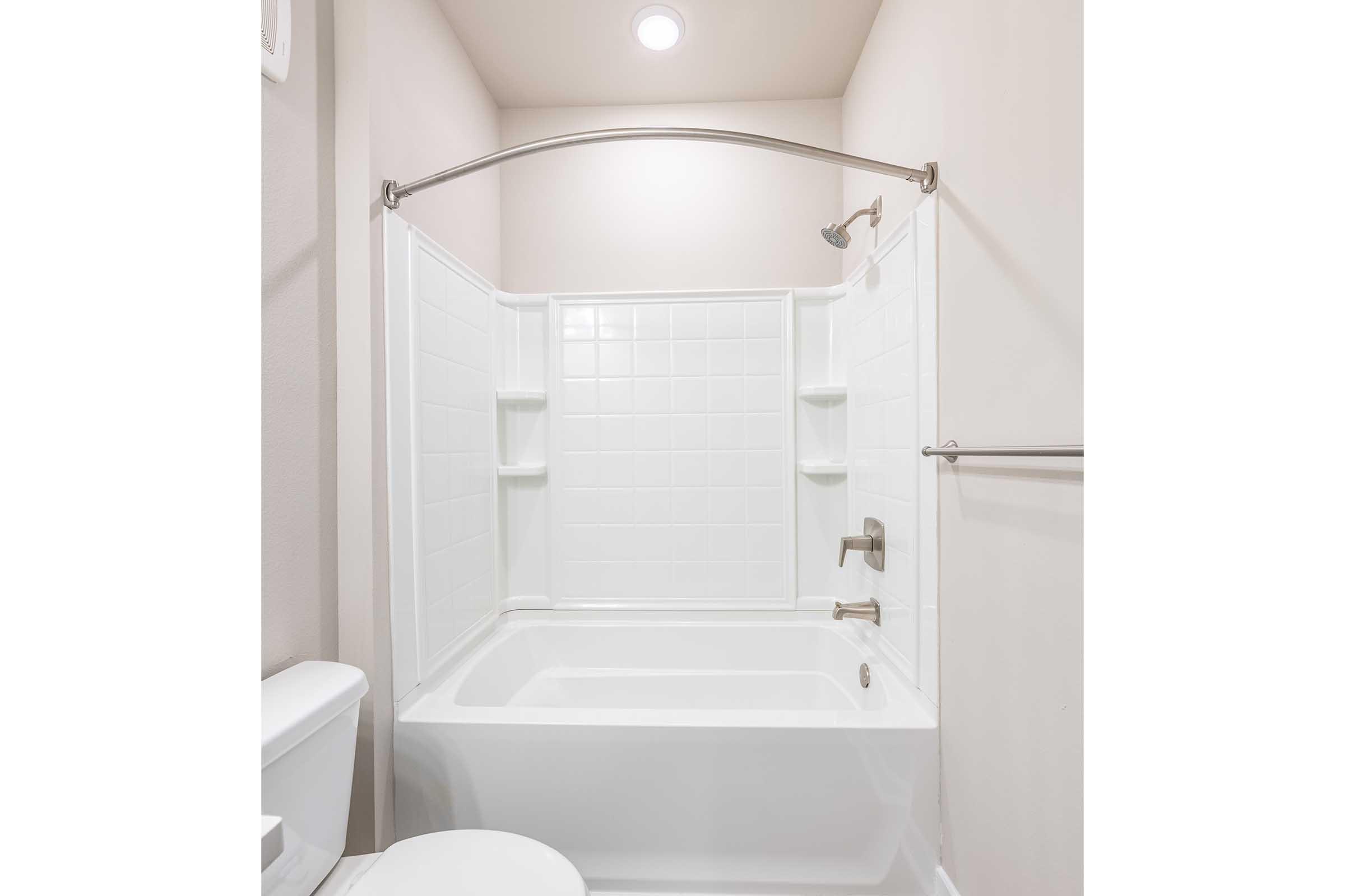 A clean and modern bathroom featuring a white tiled shower with a curved rod, a bathtub, and minimalistic fixtures. The walls are light-colored, and there's a toilet visible in the lower left corner. The overall look is bright and spacious, emphasizing a contemporary design.