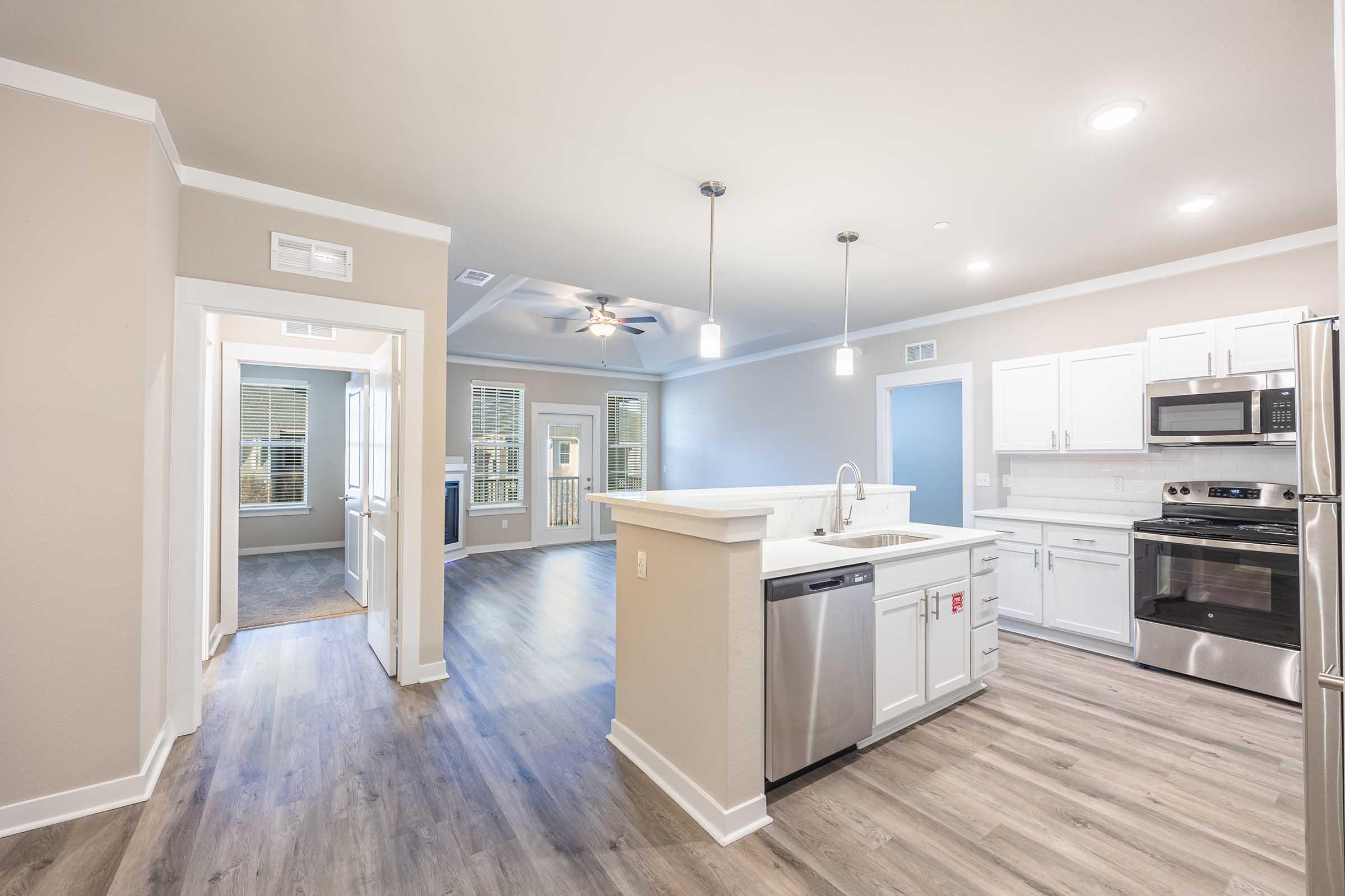 Bright, modern open-concept kitchen and living area with stainless steel appliances, quartz countertops, and ample cabinetry. Features large windows offering natural light and a ceiling fan. Doorway leads to an inviting space with views of an outdoor area. Neutral color scheme enhances the airy feel.