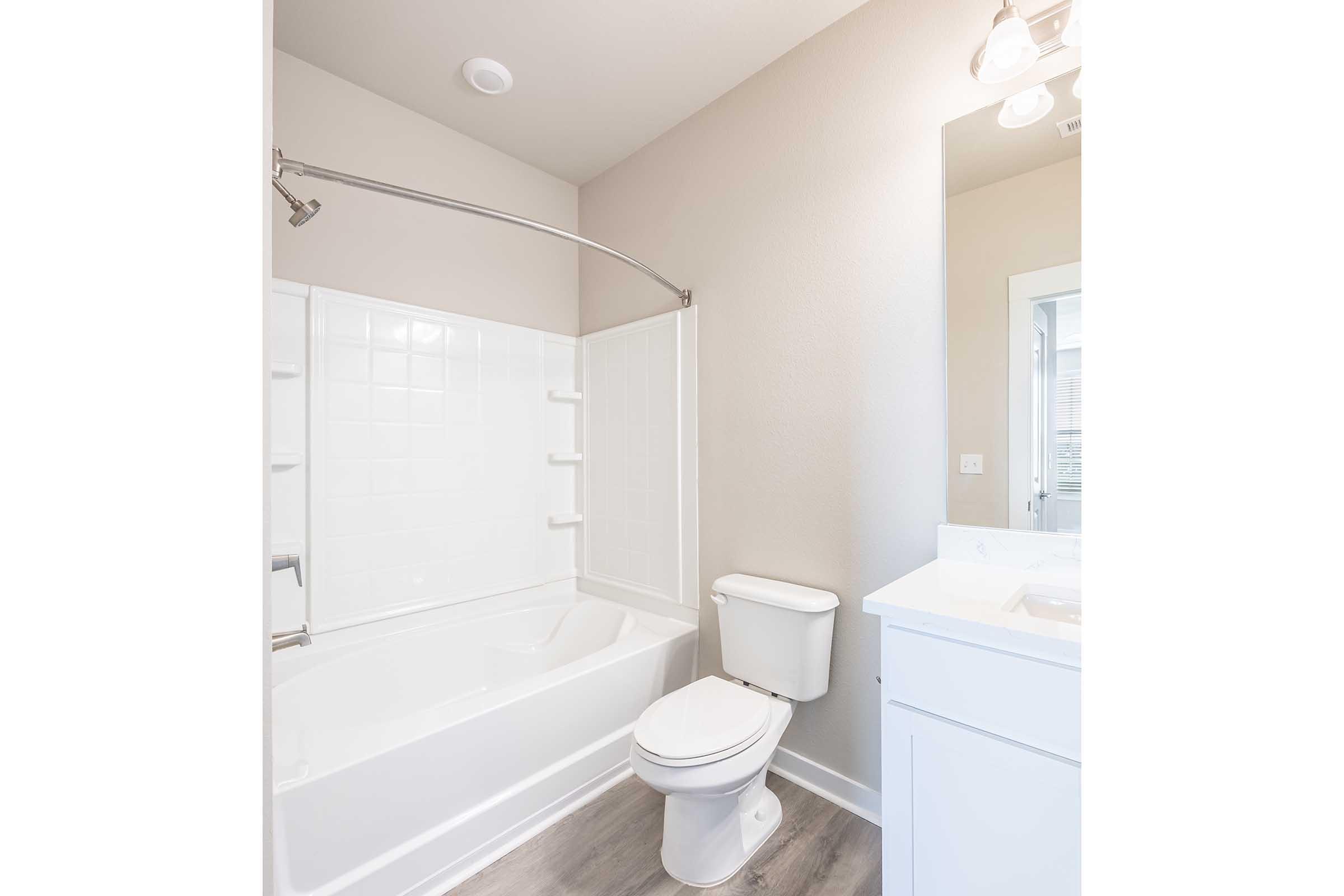 A clean and modern bathroom featuring a bathtub with an adjacent shower, a white toilet, and a vanity with a sink. The walls are painted in a soft color, and there is natural light from the doorway. The flooring is light-colored, enhancing the spacious feel of the room.