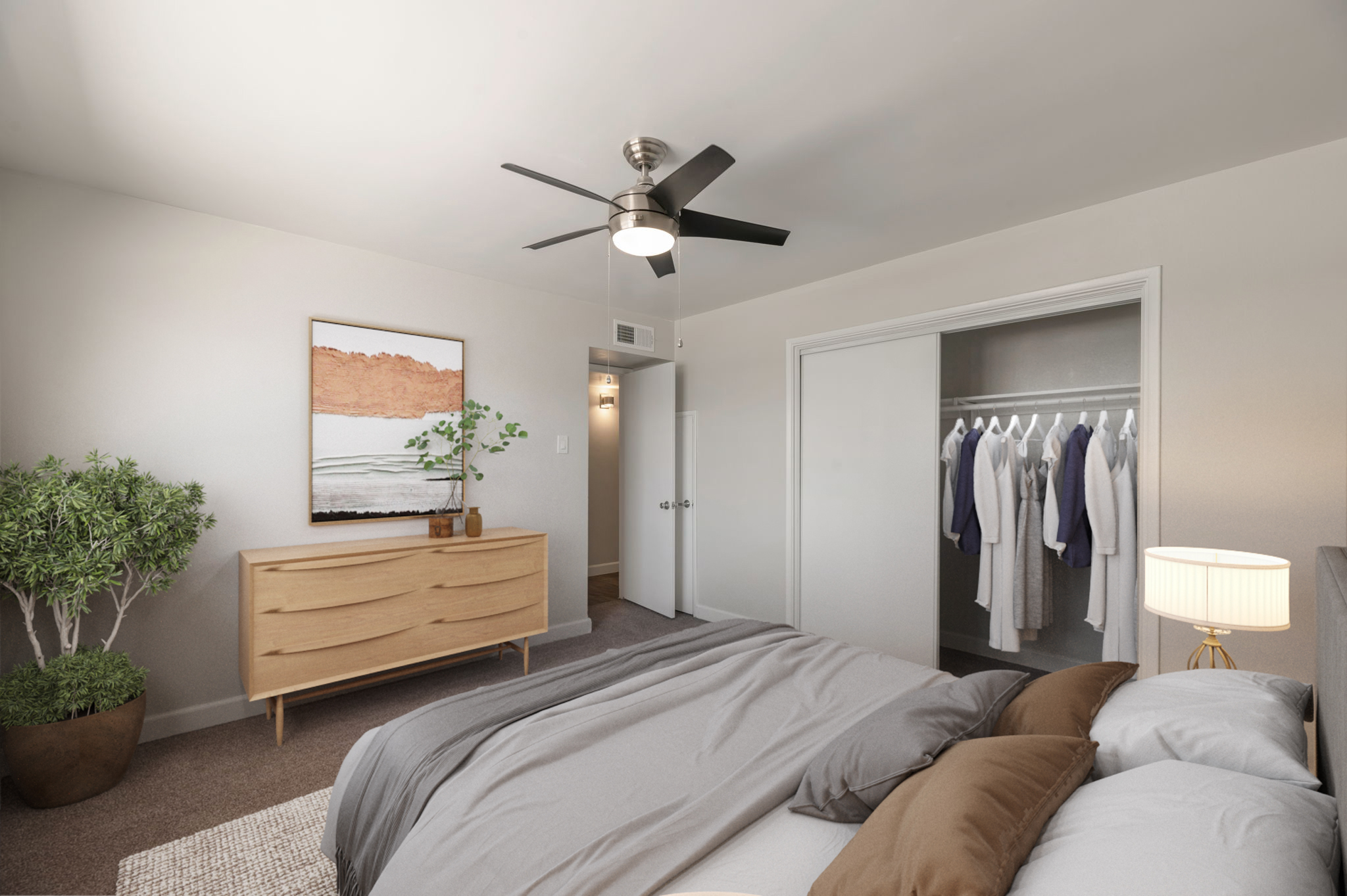 A stylish bedroom featuring a bed with gray bedding, a wooden dresser, and a potted plant. There's a fan overhead and a painting of a landscape on the wall. A closet is visible with hanging clothes, and a door leads to another room. The space is bright and modern, with neutral tones throughout.
