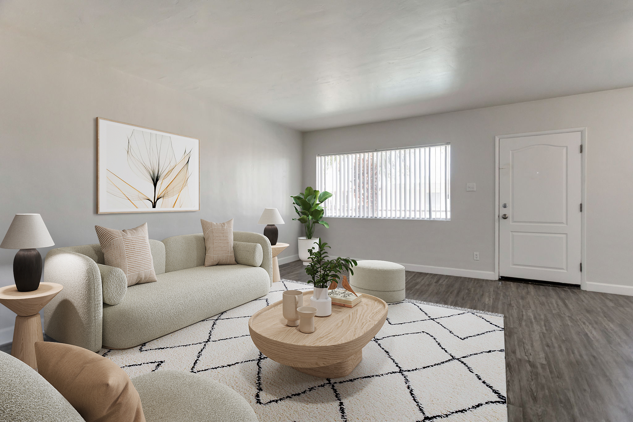A modern living room featuring a light-colored sofa, two lamps, a round coffee table, and a potted plant. The walls are neutral-toned, with a large window letting in natural light. A stylish artwork is displayed on the wall, and the flooring is dark wood, enhancing the contemporary feel of the space.