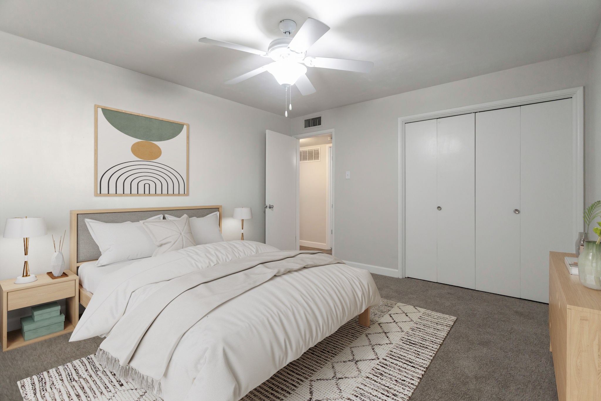 A cozy bedroom featuring a light gray color scheme, a large bed with soft bedding, a modern ceiling fan, and decorative pillows. There are two bedside lamps on wooden nightstands, a minimalist wall art above the bed, and a plush rug on the carpeted floor. A closet is visible in the background.