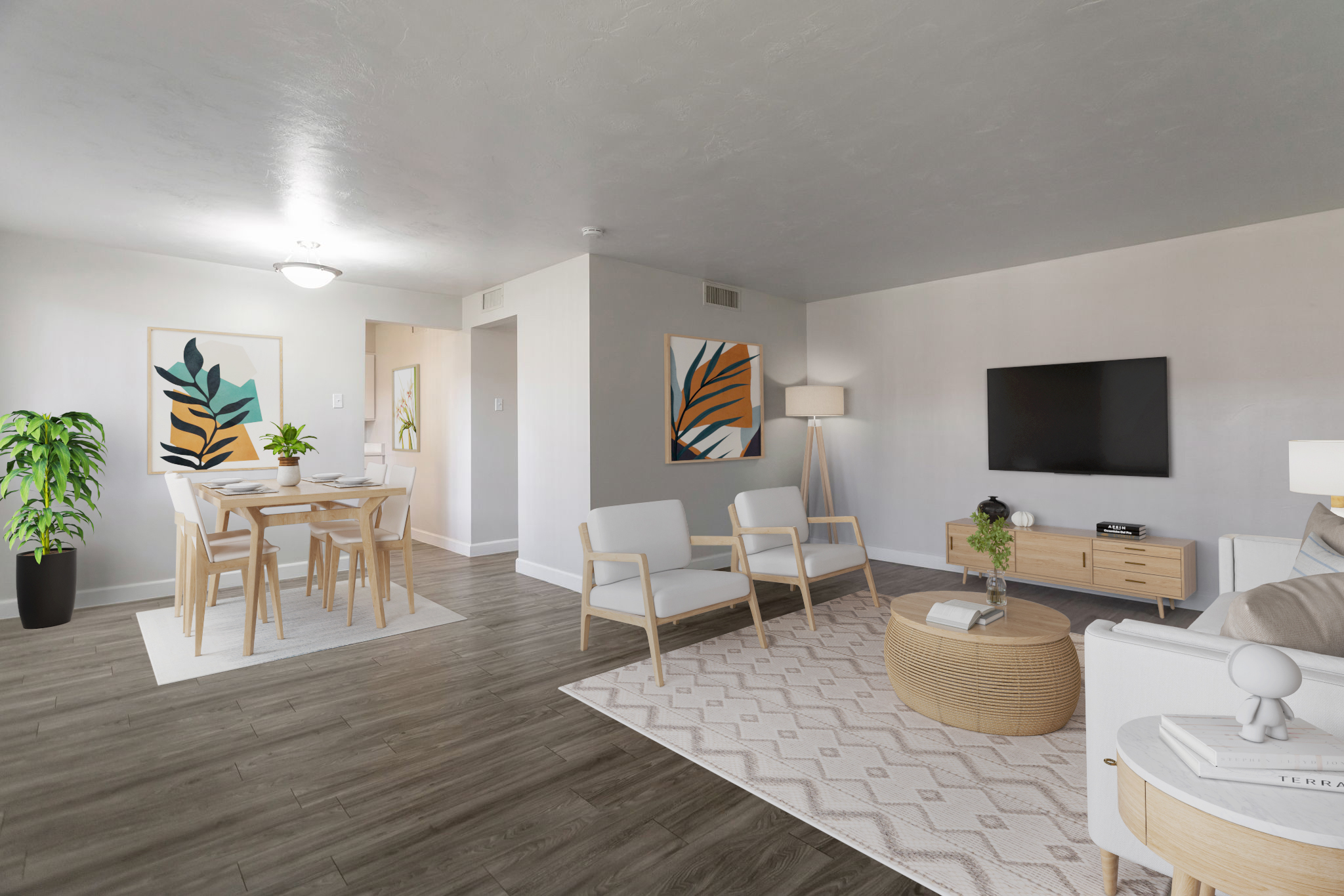 A modern living room featuring light-colored walls and wooden flooring. There are two artwork pieces with abstract leaf designs, a round coffee table, and a cozy sofa. A dining area with a table and chairs is visible, along with a potted plant and floor lamp, creating a warm and inviting atmosphere.