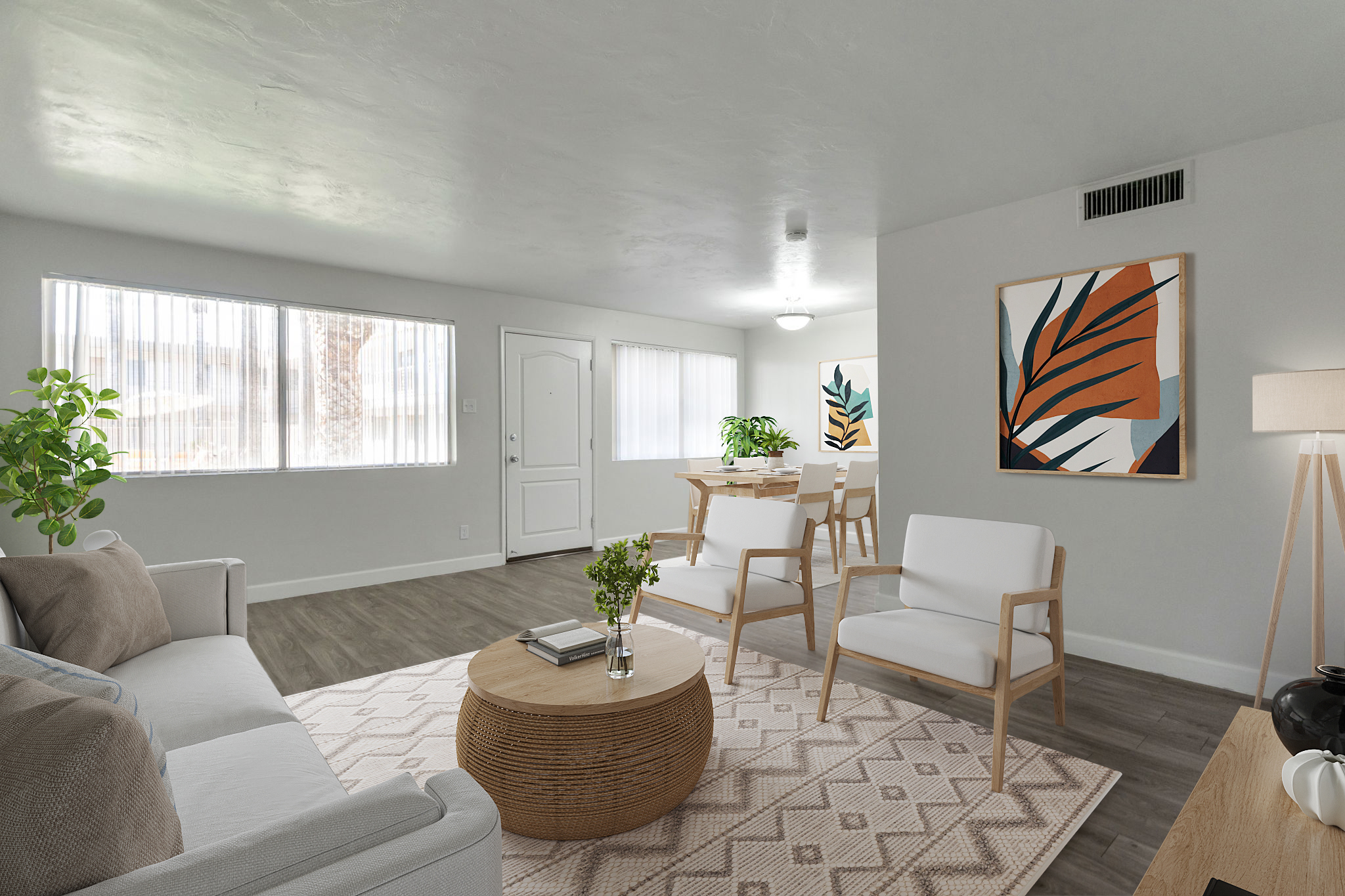 A stylish living room featuring a light-colored sofa, two white chairs, and a round rattan coffee table on a patterned rug. The room is brightly lit with natural light coming from large windows, and there are decorative plants and modern artwork on the walls, creating a welcoming atmosphere.