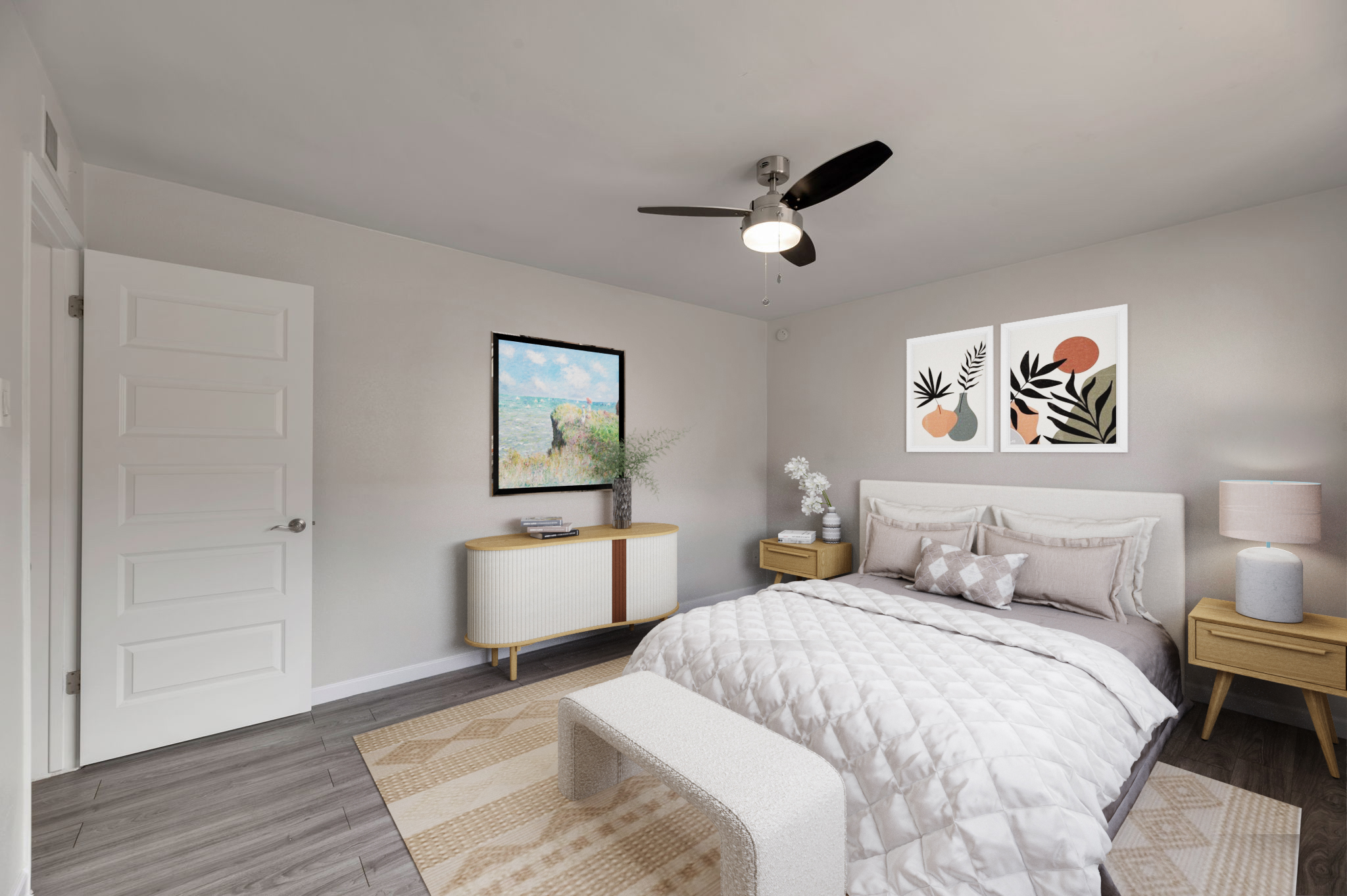 A modern bedroom featuring a queen-sized bed with a light quilt, beige bedside tables, and a decorative bench at the foot. The walls are light grey, and there's a stylish ceiling fan. Artwork with plants and soft colors adorns the wall above the bed, and a colorful landscape painting is displayed nearby. A light-colored area rug covers the floor.