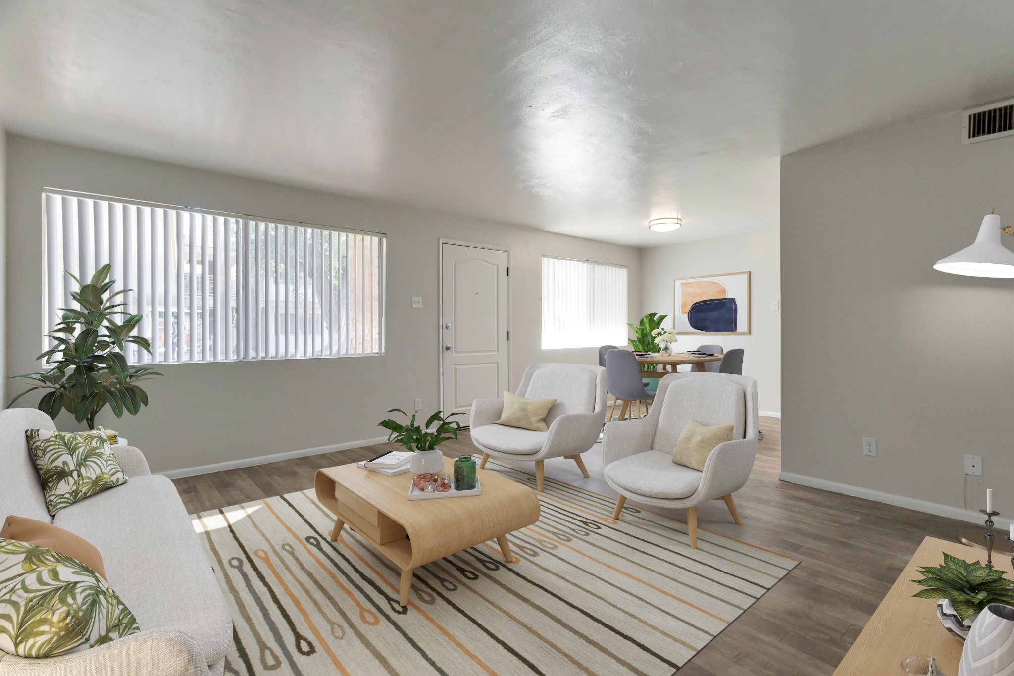 A modern living room featuring a light-colored sofa with decorative cushions, two stylish armchairs, and a wooden coffee table. The space is well-lit with large windows, plants, and a dining area in the background. The walls are neutral-colored, creating a spacious and inviting atmosphere.