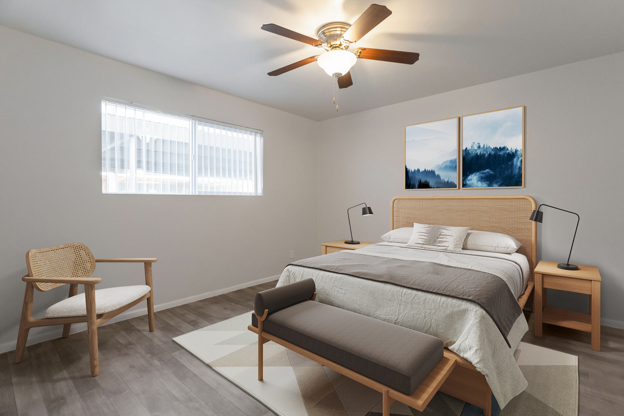 A modern bedroom featuring a queen-sized bed with a light gray and white bedding set. There are two minimalist side tables with lamps on either side of the bed. A wooden bench sits at the foot of the bed, and a light-colored chair is in the corner. The walls are painted white, and there are two framed landscape artworks above the bed.