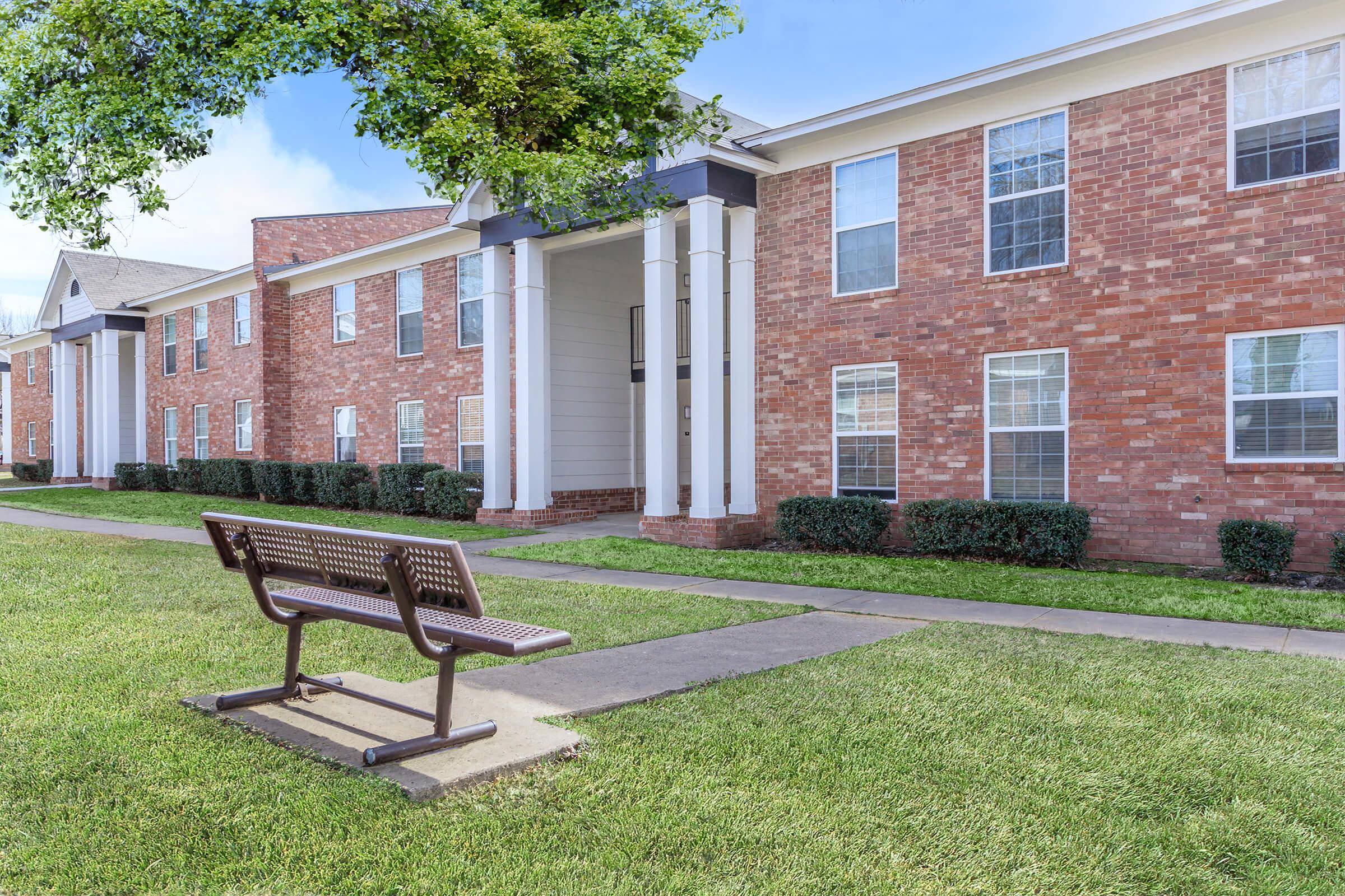 an empty park bench sitting in front of a brick building