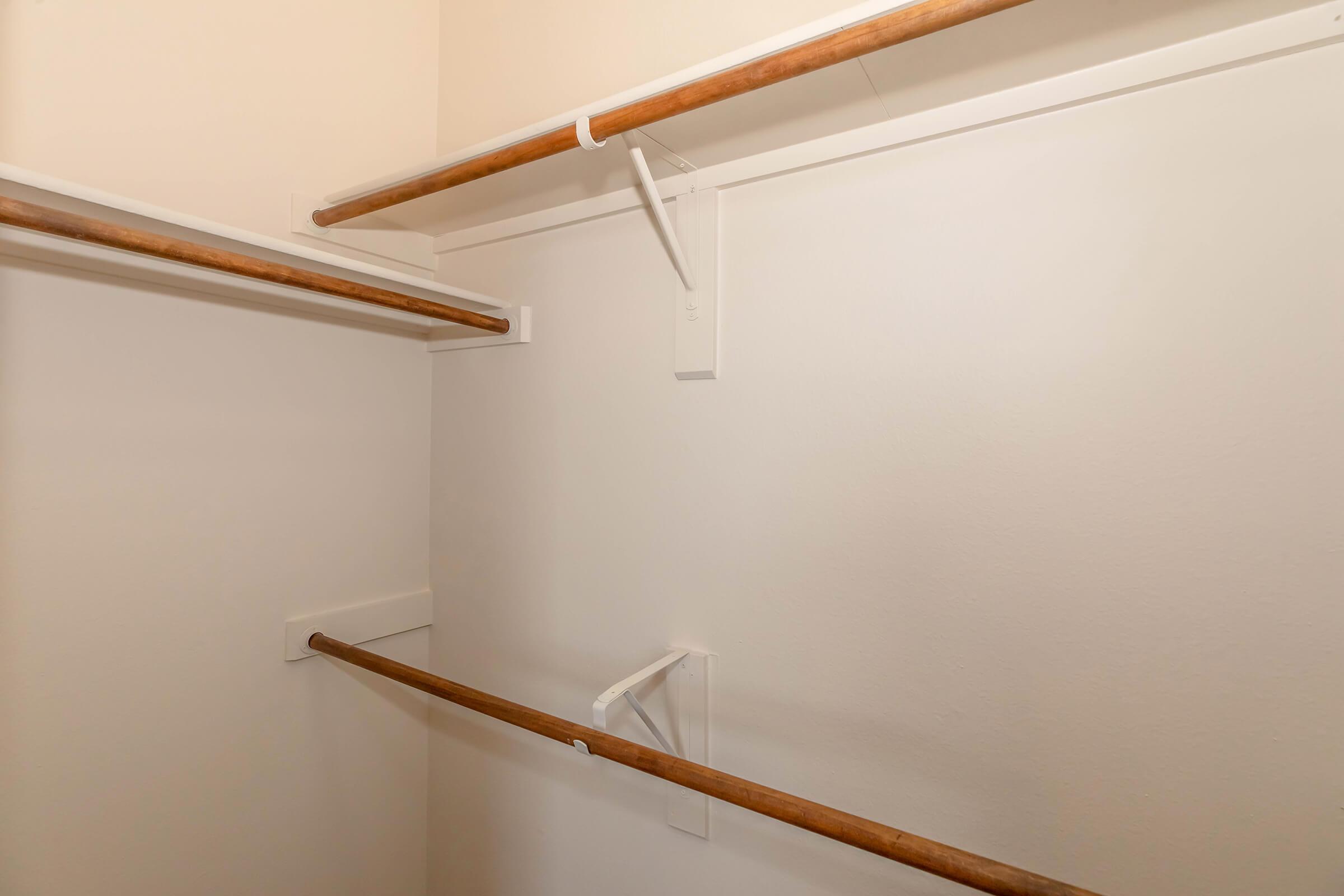 Empty closet with two wooden hanging rods mounted on white walls. There are wall brackets holding the rods, and the space is well-lit, suggesting it's a functional storage area. The overall appearance is clean and minimalistic.