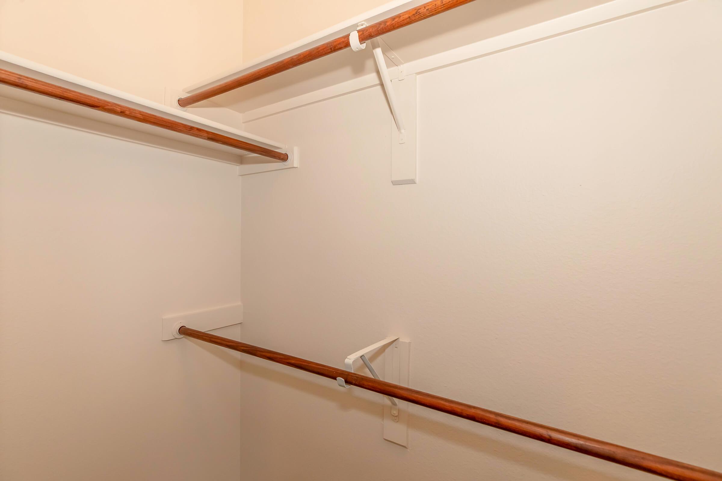 Empty closet space featuring two wooden clothing rods attached to white walls. The rods are supported by white brackets, highlighting a clean and minimalistic storage area.