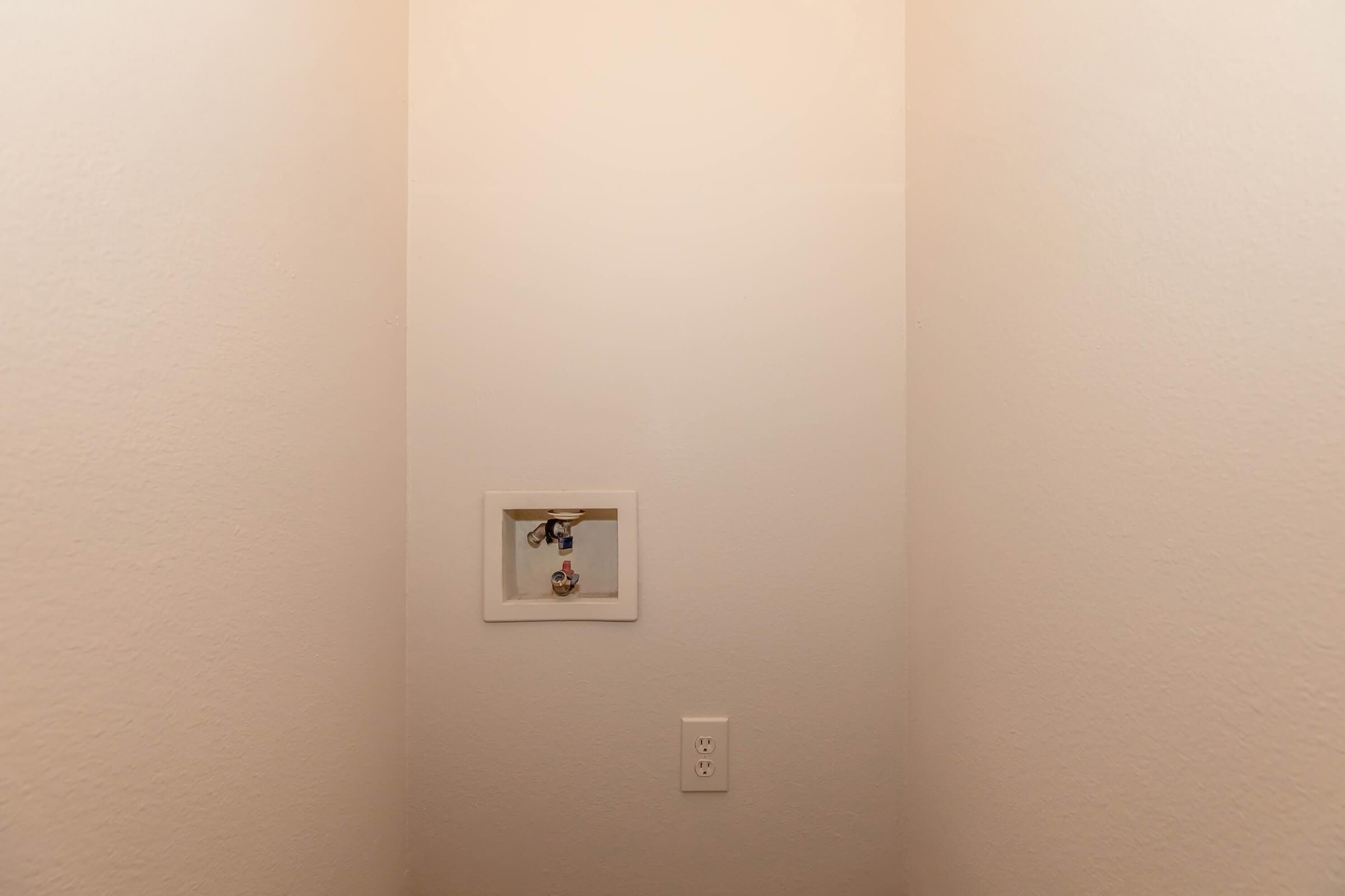 A plain, well-lit corner of a room with white walls. There is a small framed item on the wall, possibly a light switch or decorative piece. The space appears tidy and minimalistic, focusing on the simplicity of the design.