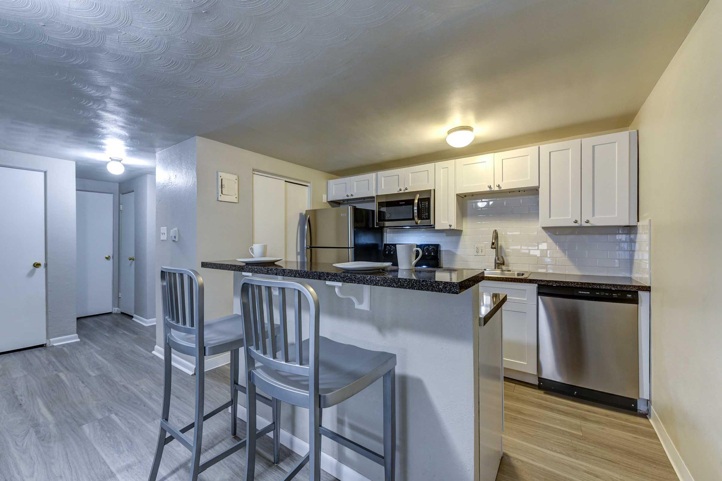 Modern kitchen interior featuring white cabinetry, stainless steel appliances, and a black granite countertop.