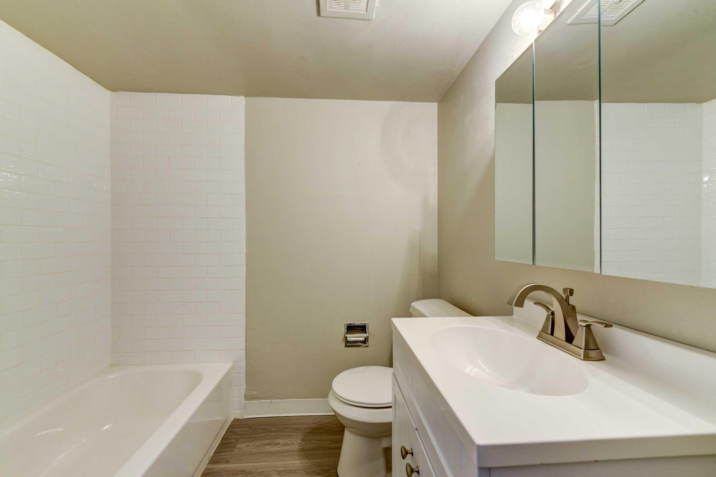 A clean, modern bathroom featuring a white bathtub and shower with tiled wall, a white sink with a stylish faucet, a mirror above the sink, and neutral-colored walls. 