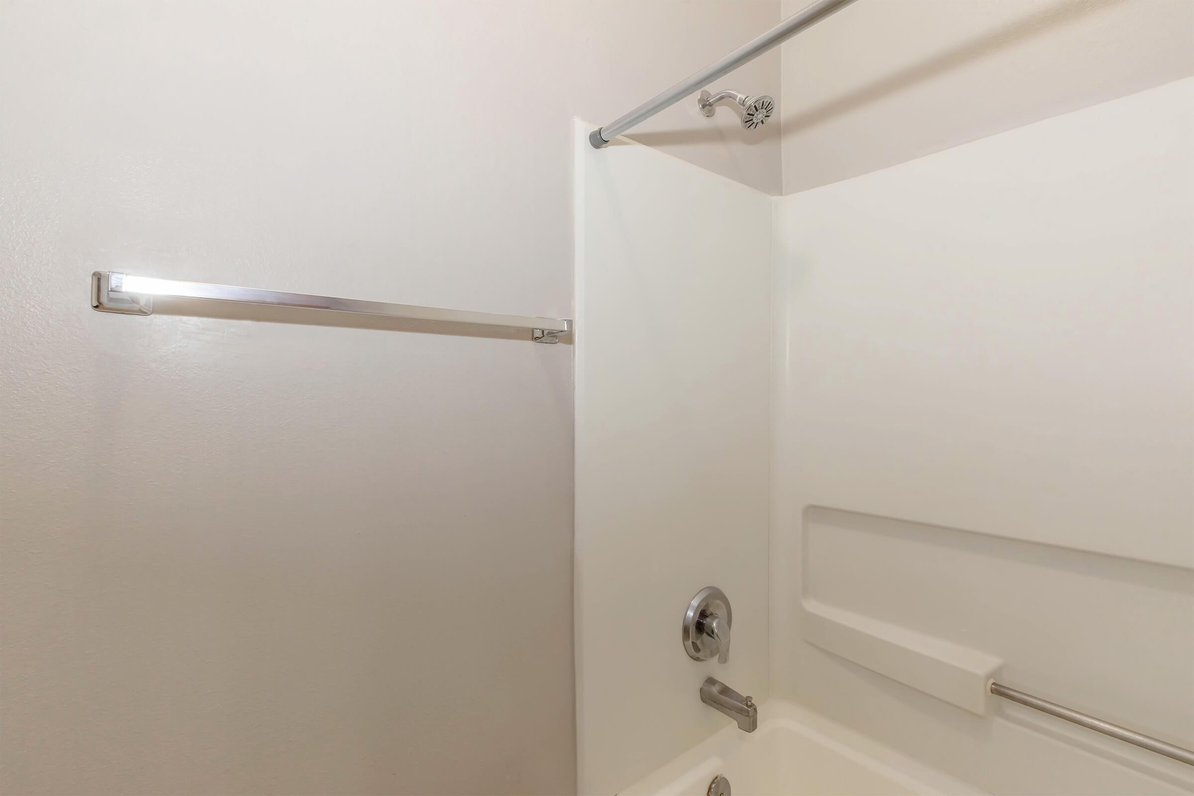 A clean and minimalist bathroom featuring a shower area with a chrome showerhead, a soap dish built into the wall, and a towel bar. The walls are white, enhancing the bright and spacious appearance of the space.