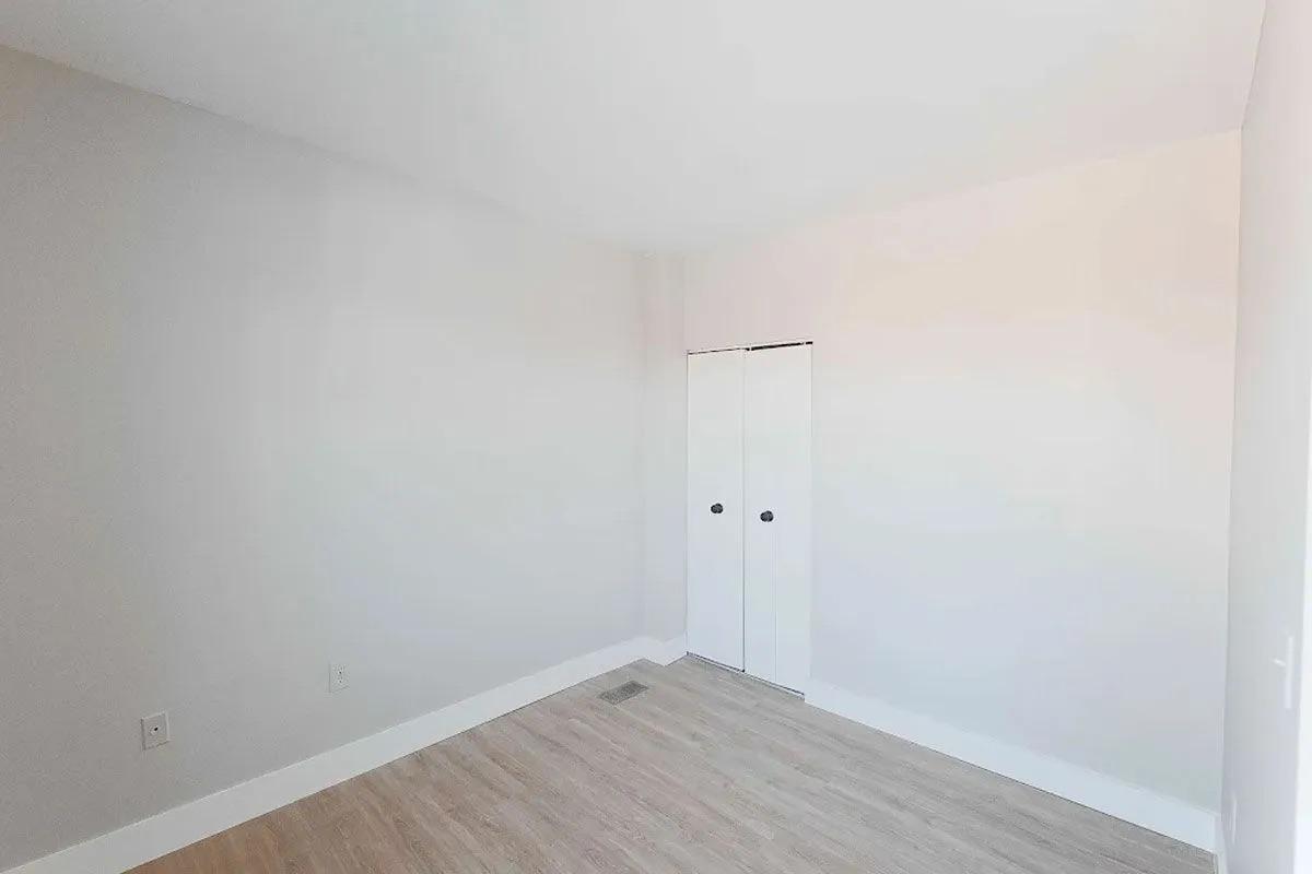 A bright and empty room with light-colored walls and wooden flooring. There is a sliding closet door on one wall, and the space appears clean and sparsely furnished, creating a minimalist aesthetic. Natural light may be coming from a window not visible in the image.