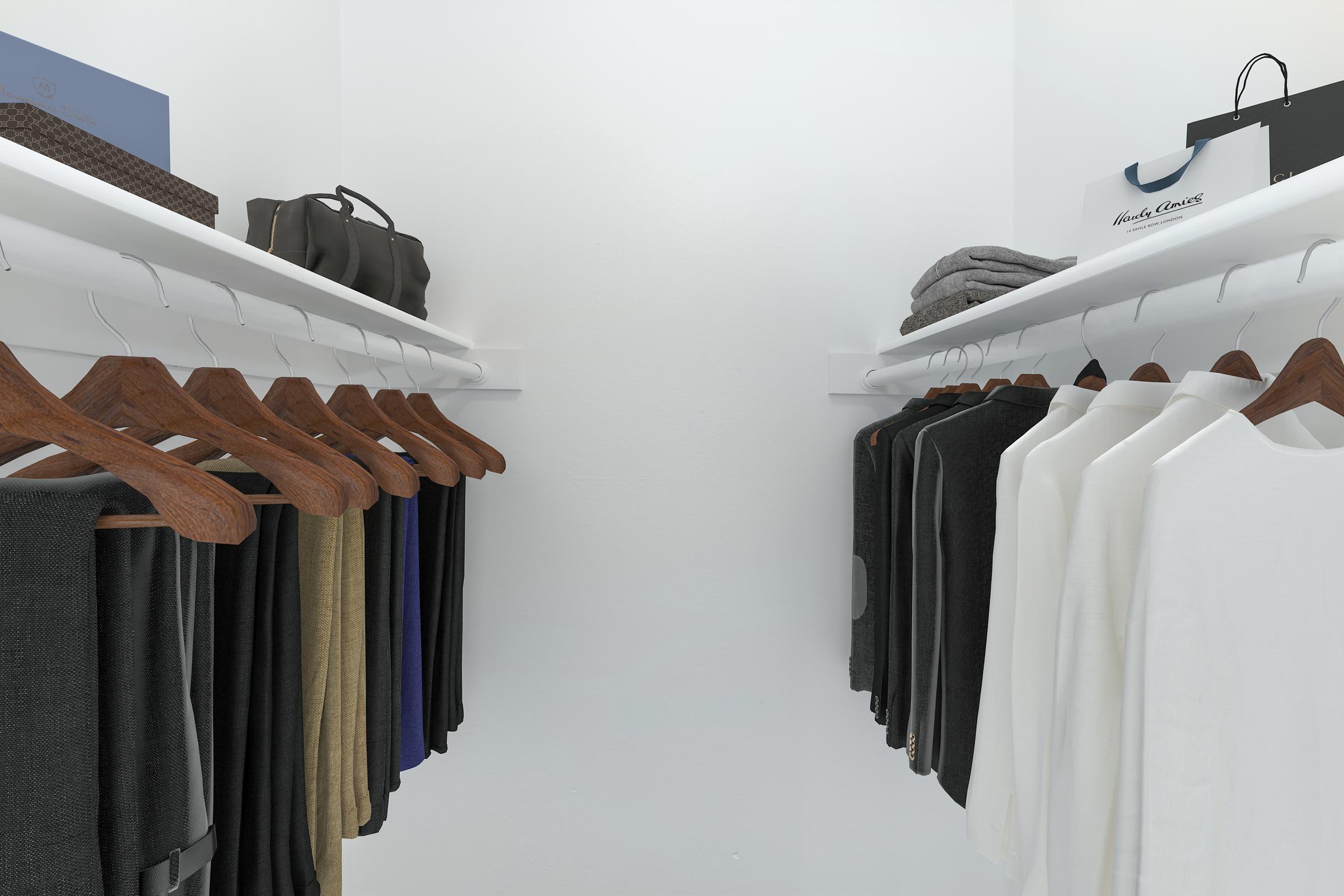 A neatly organized closet featuring multiple hanging garments on wooden hangers, including various tops in dark and light colors. On the shelves above, there are folded towels and bags, creating a tidy and minimalist storage space. The walls are white, enhancing the clean aesthetic.