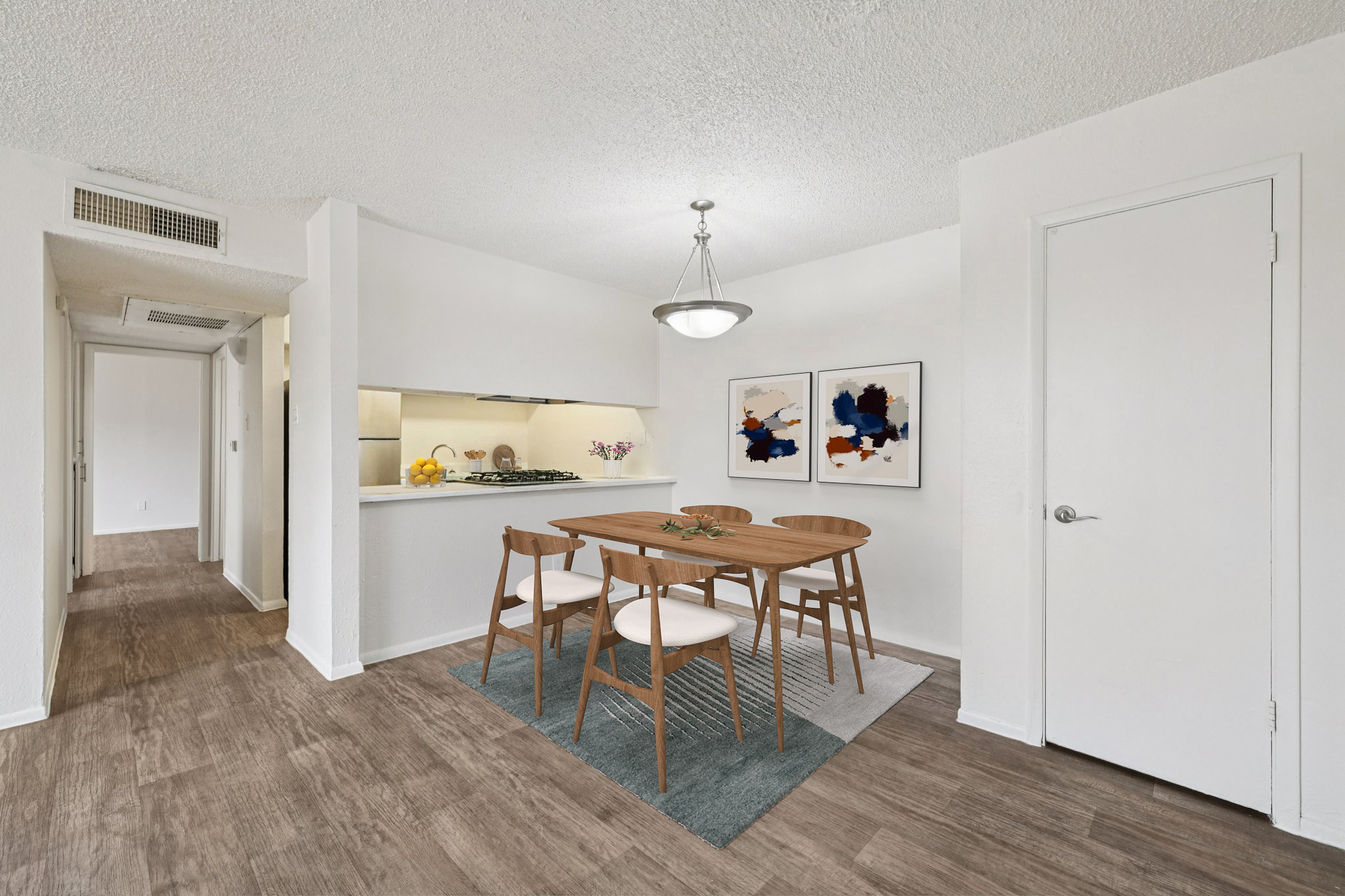 Bright and modern dining area with a wooden table and white chairs, surrounded by neutral-toned walls. A well-lit kitchen features a bar, while abstract art decorates the walls. The space has a warm, inviting atmosphere with natural light streaming in. Hardwood flooring completes the contemporary look.