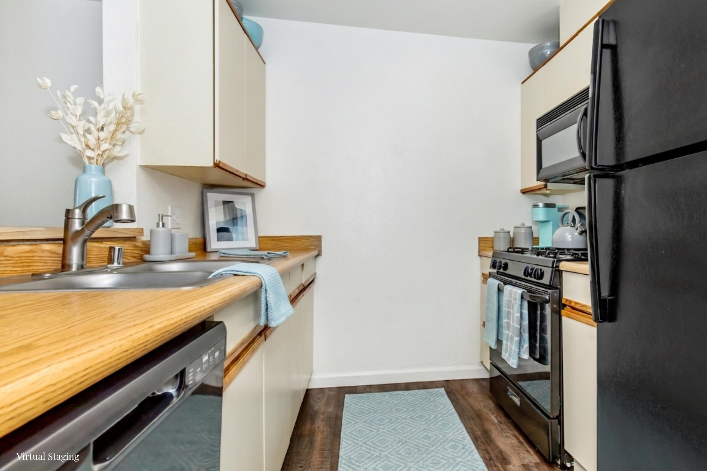 A modern kitchen featuring light-colored cabinets and wooden countertops. The space includes a stainless steel sink, a black refrigerator, and a gas stove. Decorative elements include a blue rug and kitchen accessories, creating a bright and inviting atmosphere.