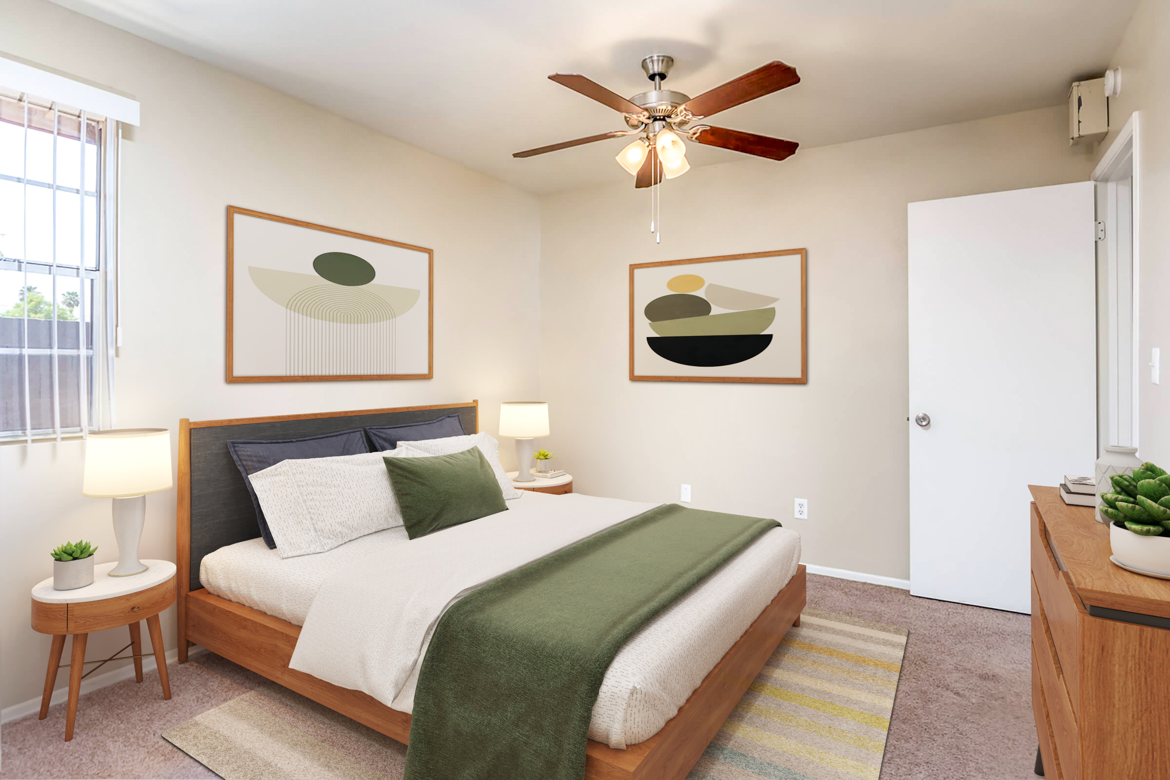 A cozy bedroom featuring a queen-sized bed with a green throw blanket and decorative pillows. The walls are adorned with abstract art, and there are two bedside lamps on wooden side tables. A ceiling fan provides airflow, and a dresser with plants adds a touch of greenery. A door and a window let in natural light.