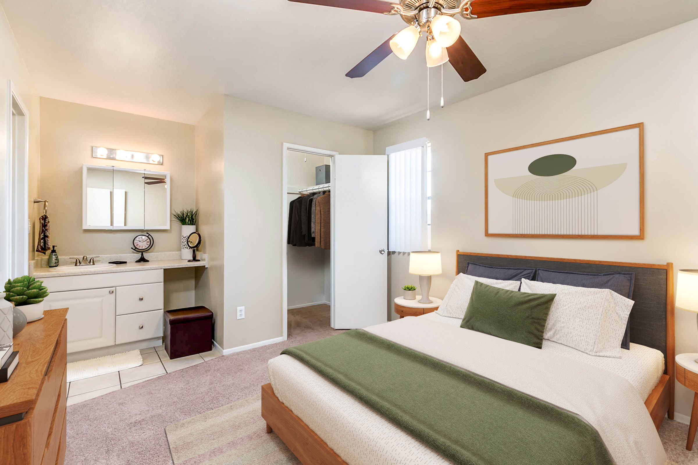 A cozy bedroom featuring a wooden bed with green and white bedding, a bedside table with lamps, and a large window. A dressing area with a mirror and closet is visible, along with a simple artwork on the wall. The room has neutral wall colors and soft carpeting, creating a warm and inviting atmosphere.