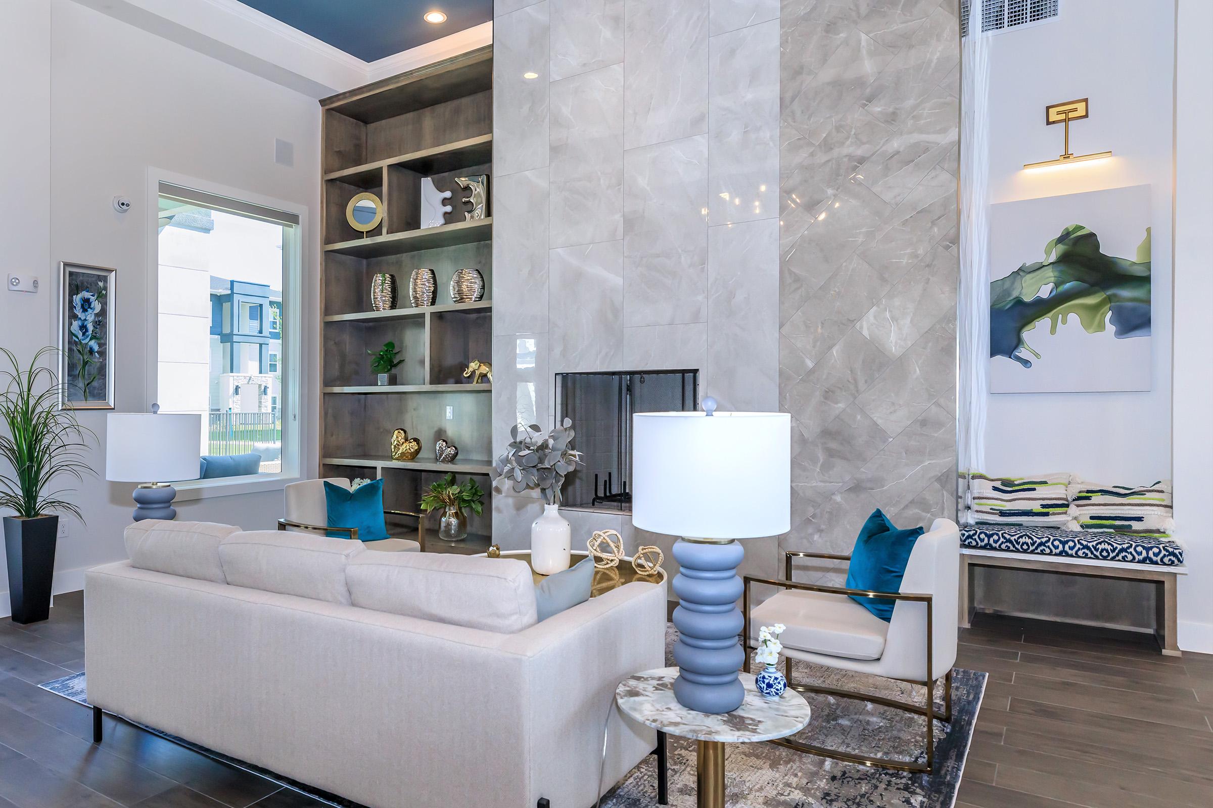 A modern living room featuring a stylish sofa and elegant armchairs. A sleek marble accent wall hosts a decorative shelf with various items. There's a large window allowing natural light, complemented by a potted plant and contemporary lamps. The space combines comfort and sophistication with neutral tones and artistic decor.