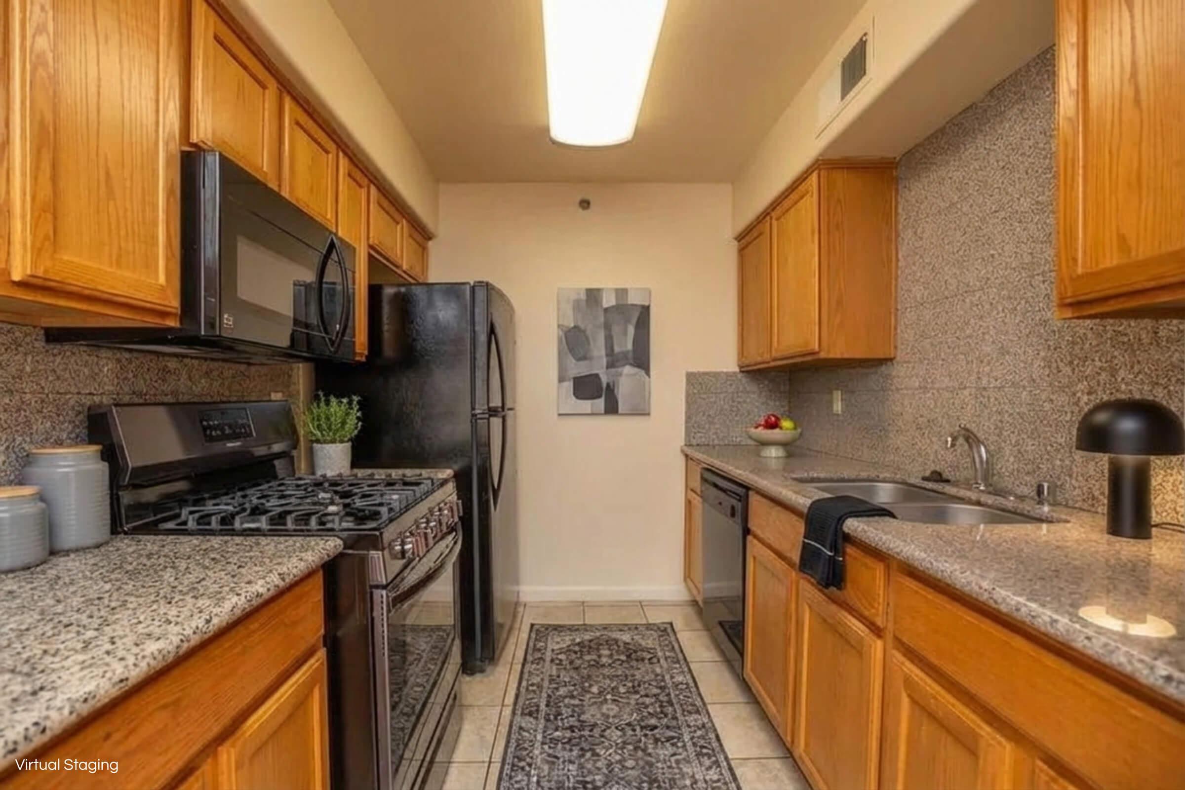 Modern kitchen featuring wooden cabinets, granite countertops, and stainless steel appliances. Includes a gas stove, microwave, black refrigerator, and dishwasher. A small decorative rug and a bowl of fruit add a touch of warmth, while a piece of artwork adorns the wall. Well-lit with overhead lighting.
