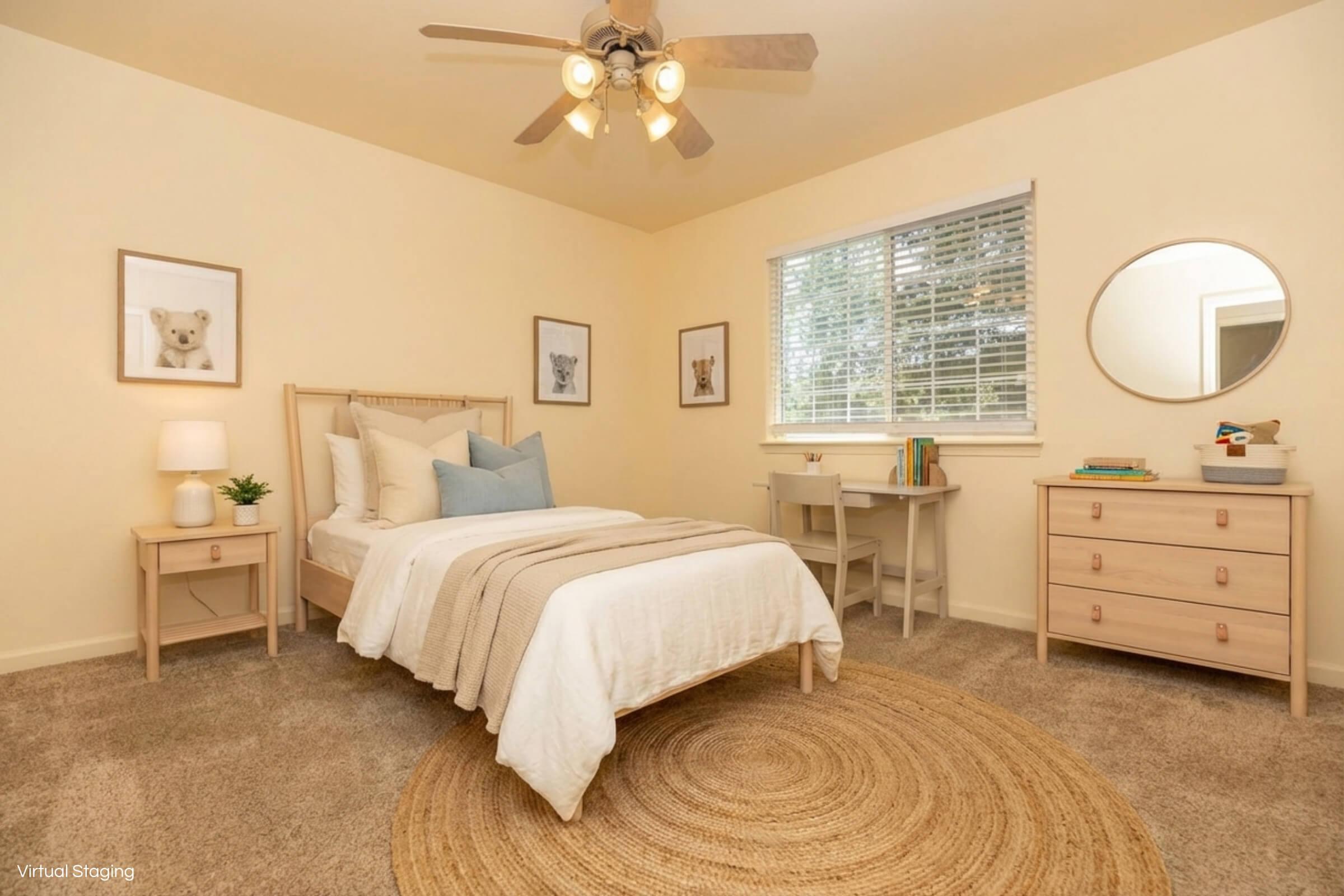 Cozy bedroom featuring a light-colored bed with a neutral blanket and decorative pillows, a circular rug, a wooden dresser, a small desk, and framed animal artwork on the walls. A window allows natural light, and a ceiling fan adds to the airy feel of the space.