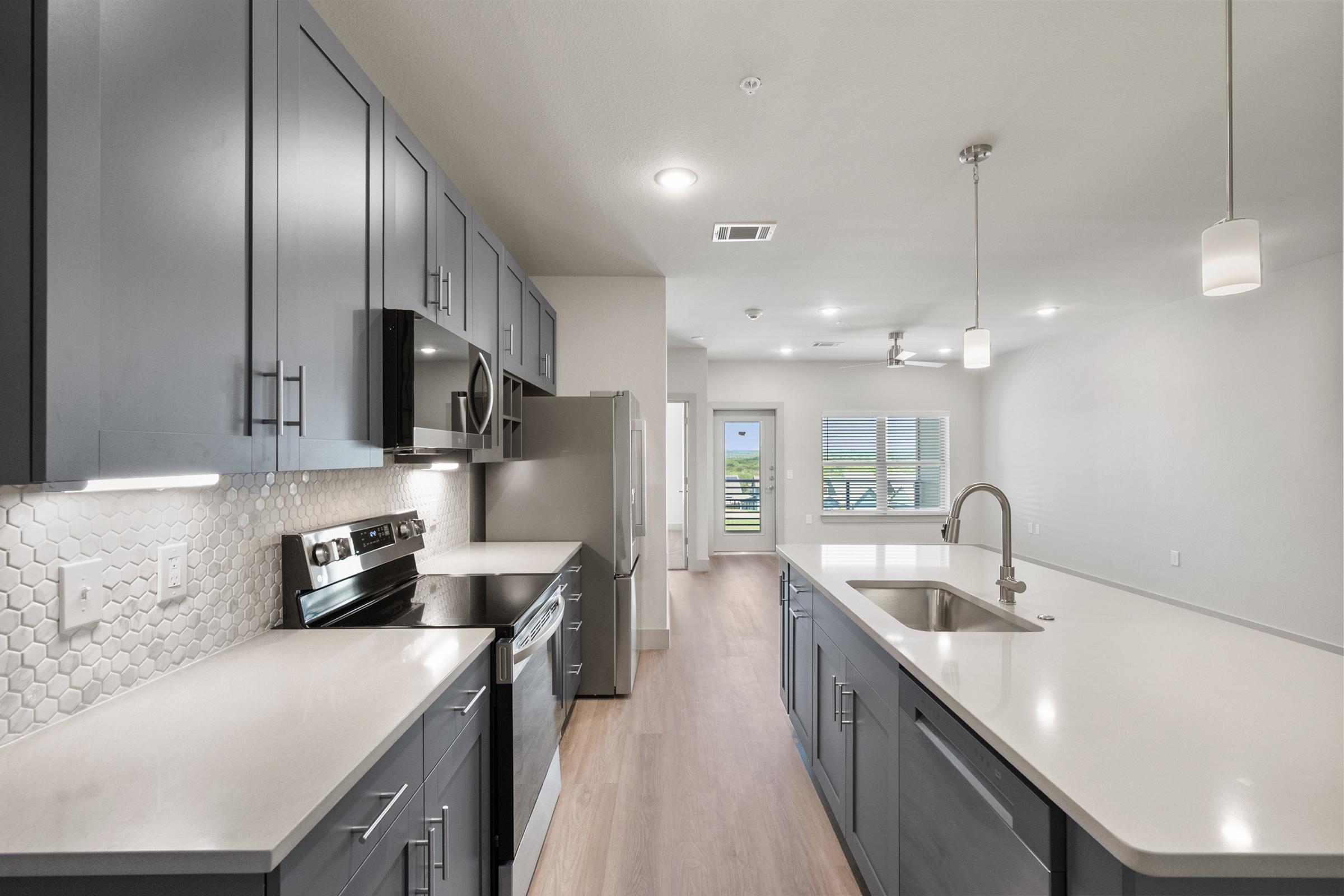 Modern kitchen featuring pendant lighting, quartz countertops, and stainless steel appliances in the A3 one-bedroom unit.
