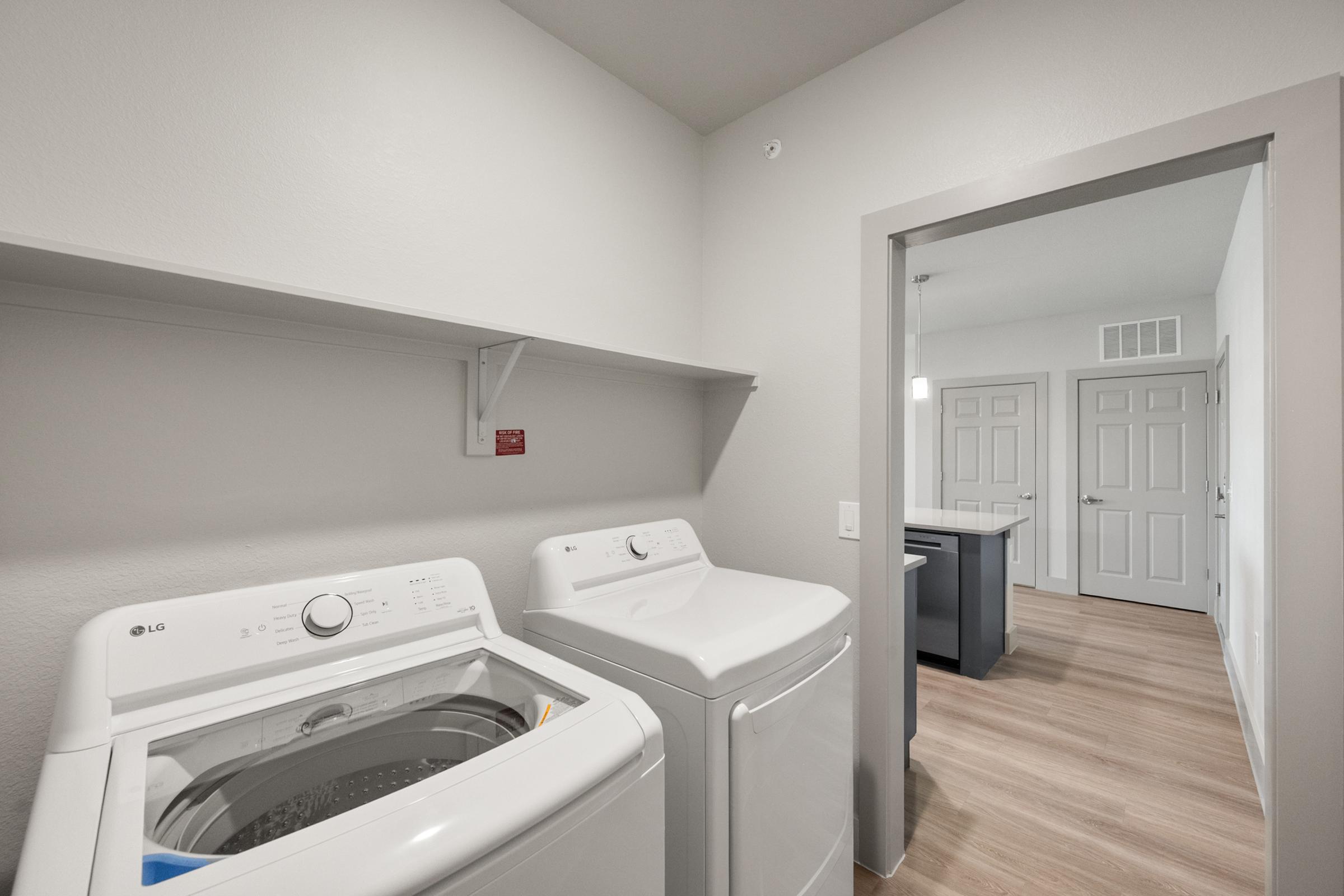 Laundry area in the A3 Floor Plan at The Emma Apartments featuring a full-size washer and dryer within the unit, along with built-in shelving for storage.