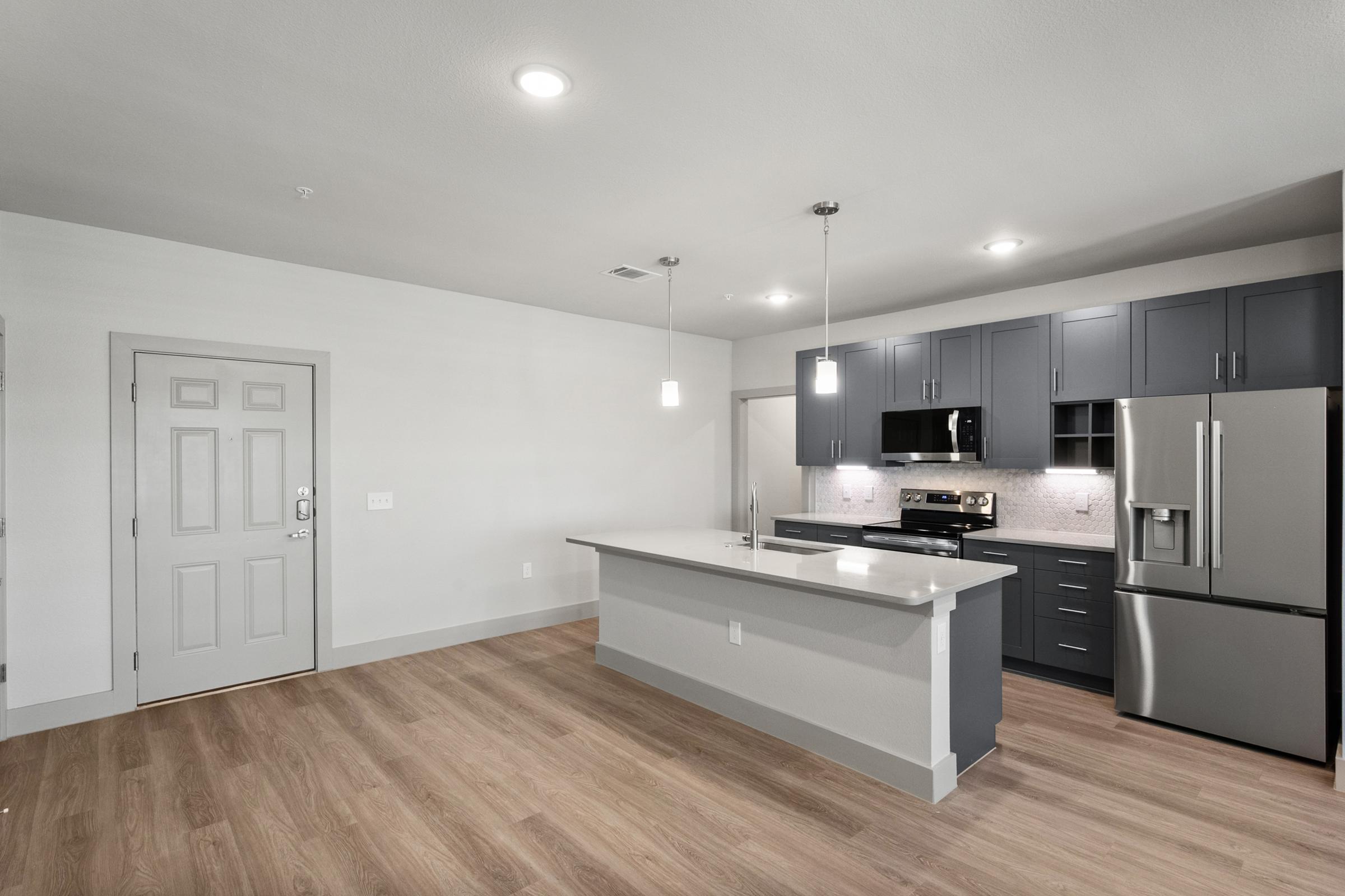 Modern kitchen in the B1 Floor Plan with stainless steel appliances, quartz countertops, pendant lighting, and an open layout flowing into the living area.