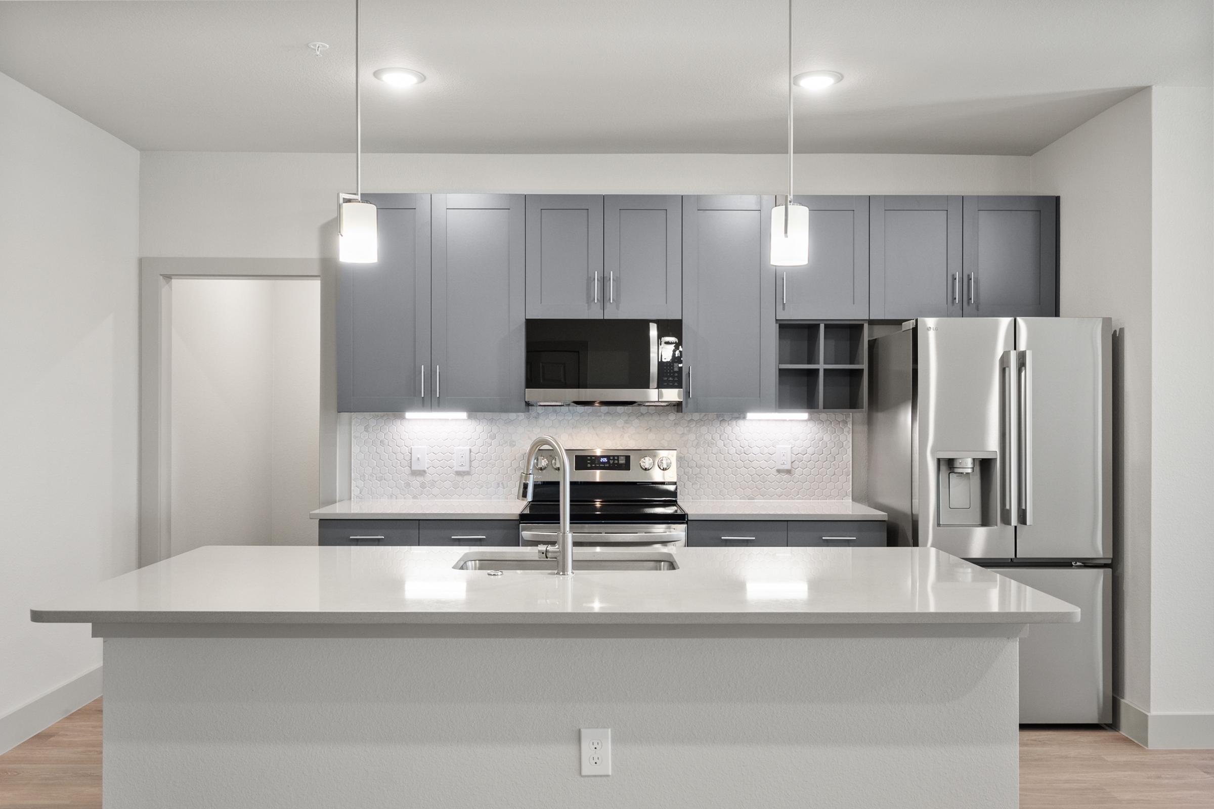 Modern kitchen in the B1 Floor Plan with stainless steel appliances, quartz countertops, pendant lighting, and an open layout flowing into the living area.