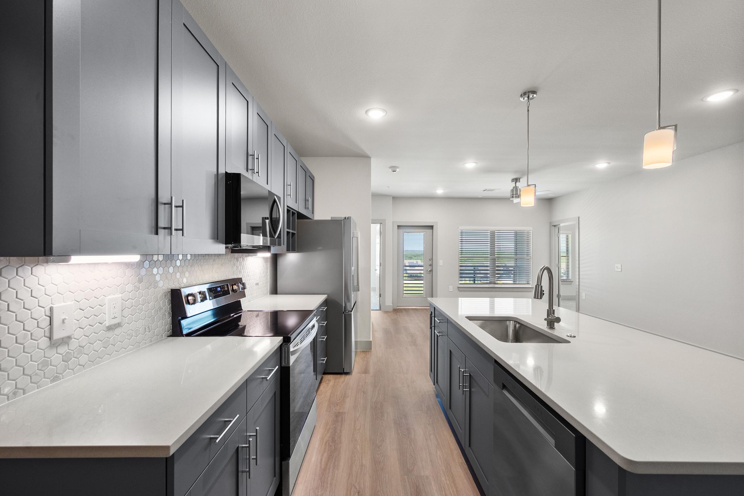 Modern kitchen in the B1 Floor Plan with stainless steel appliances, quartz countertops, pendant lighting, and an open layout flowing into the living area.