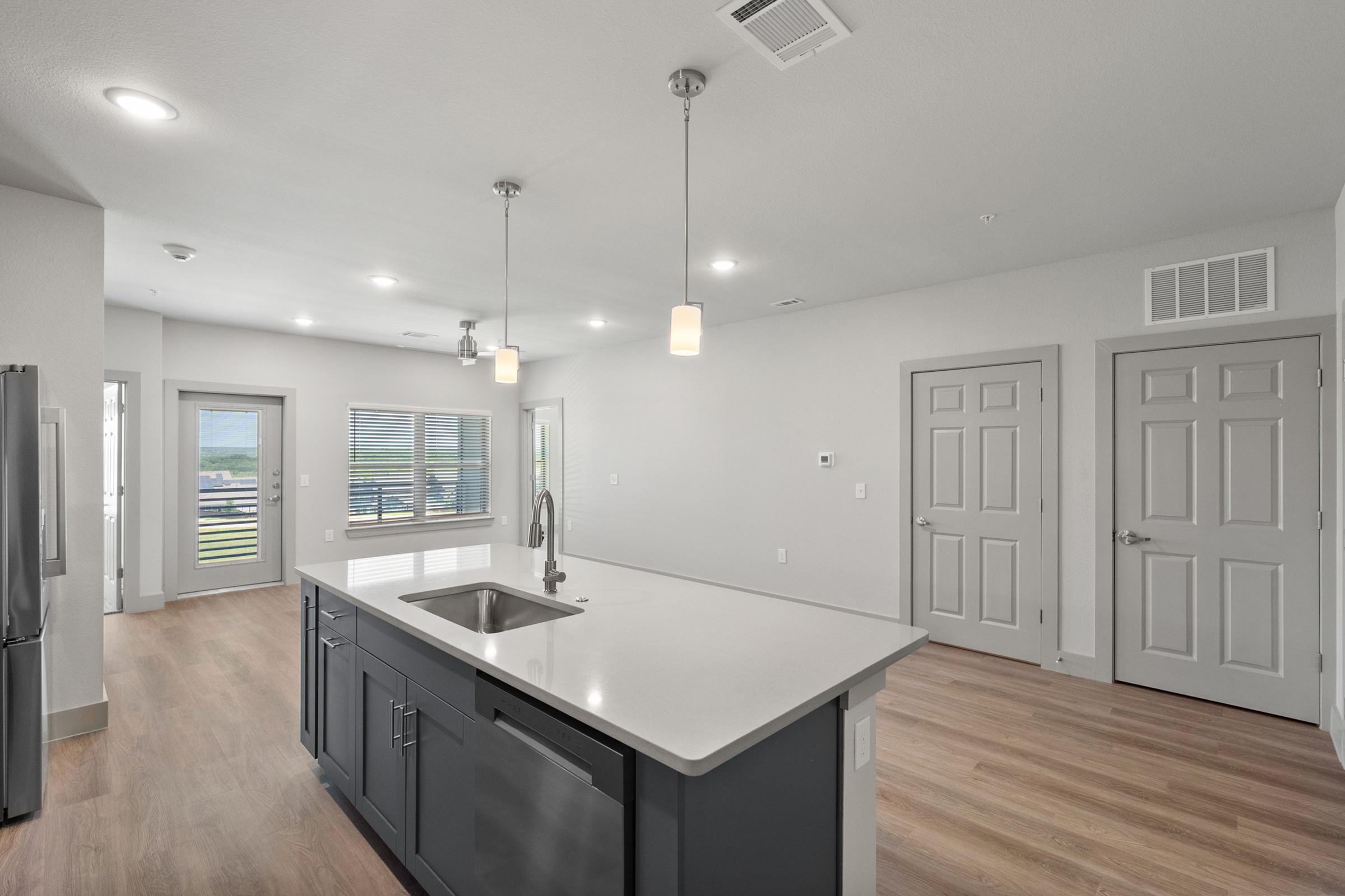 Modern kitchen in the B1 Floor Plan with stainless steel appliances, quartz countertops, pendant lighting, and an open layout flowing into the living area.
