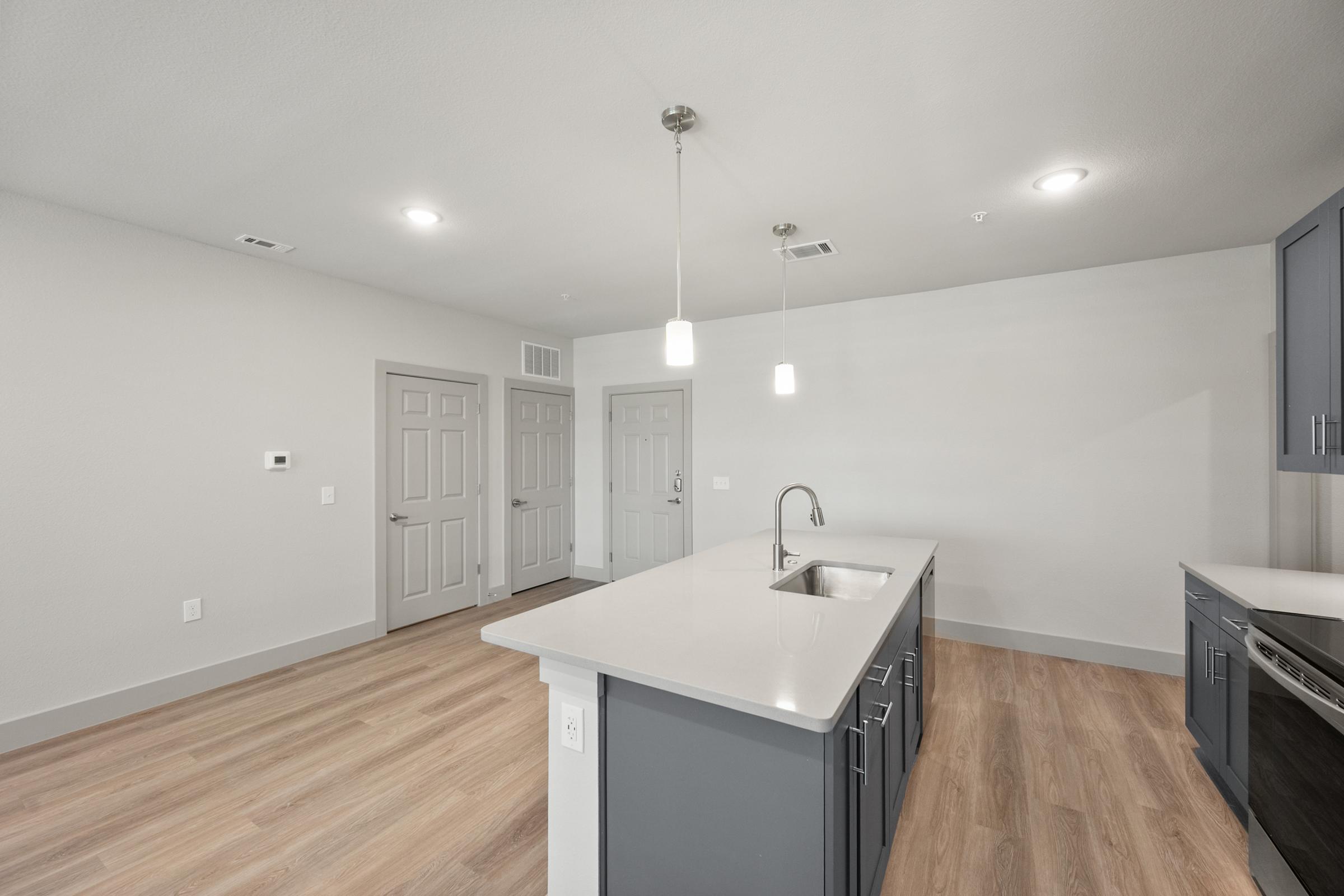 Modern kitchen in the B1 Floor Plan with stainless steel appliances, quartz countertops, pendant lighting, and an open layout flowing into the living area.