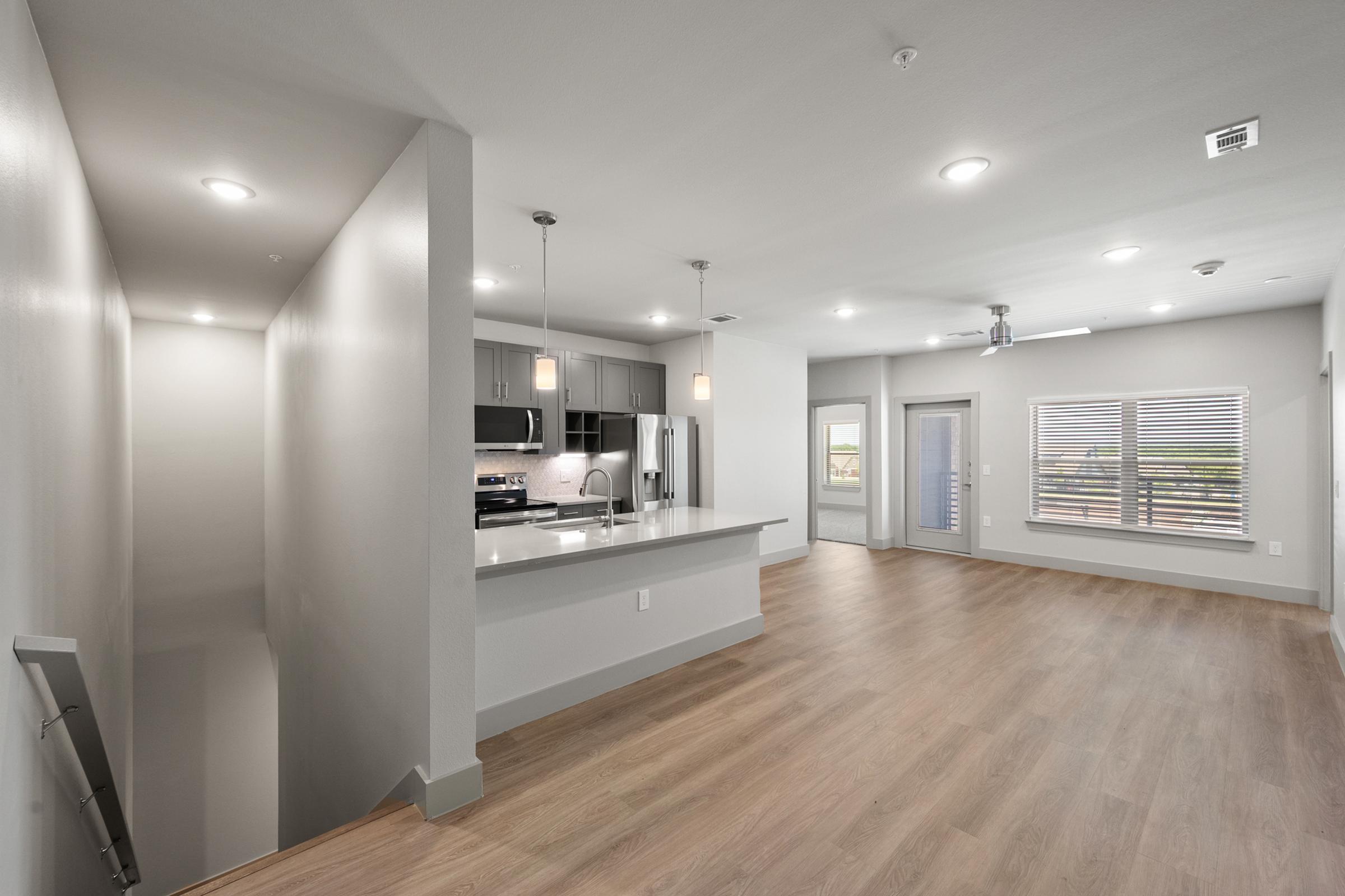 Bright and open kitchen and living area in the B2 Floor Plan at The Emma Apartments, featuring quartz countertops, stainless steel appliances, and spacious layout perfect for modern living.
