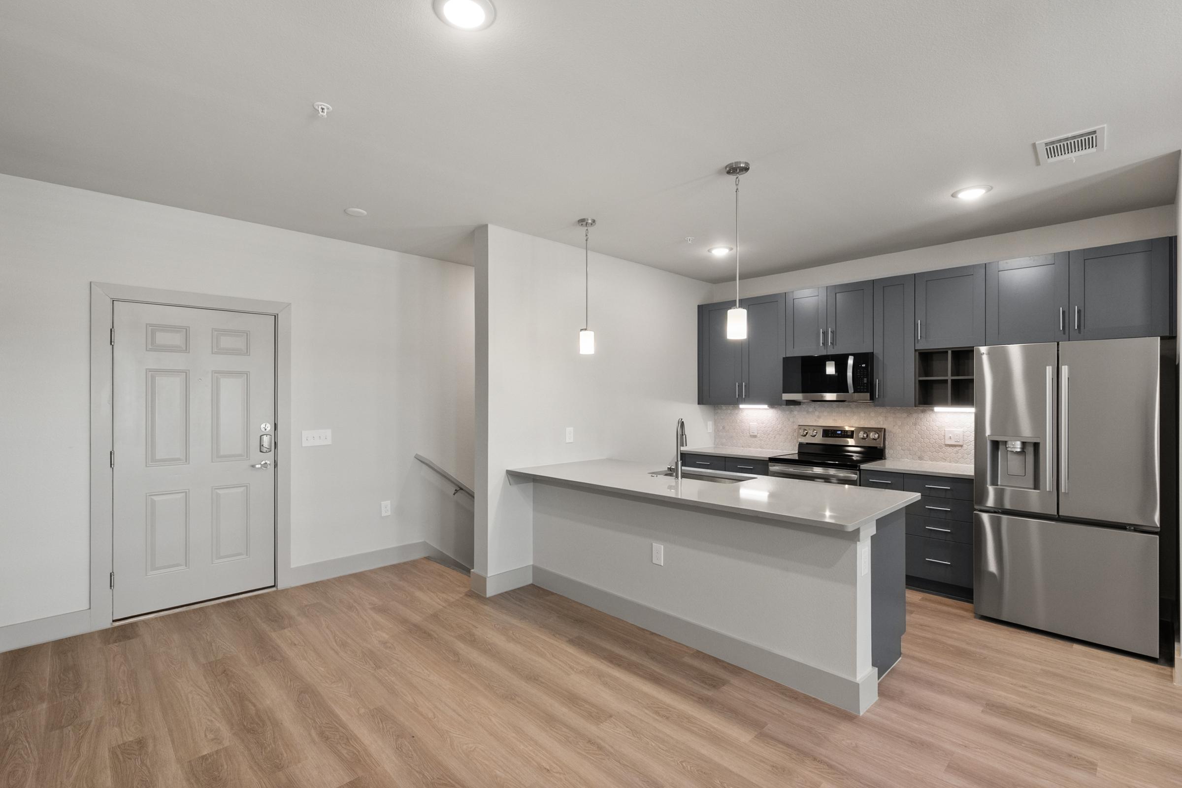 Modern kitchen in the B2 Floor Plan with stainless steel appliances, quartz countertops, pendant lighting, and a large island perfect for cooking and entertaining.