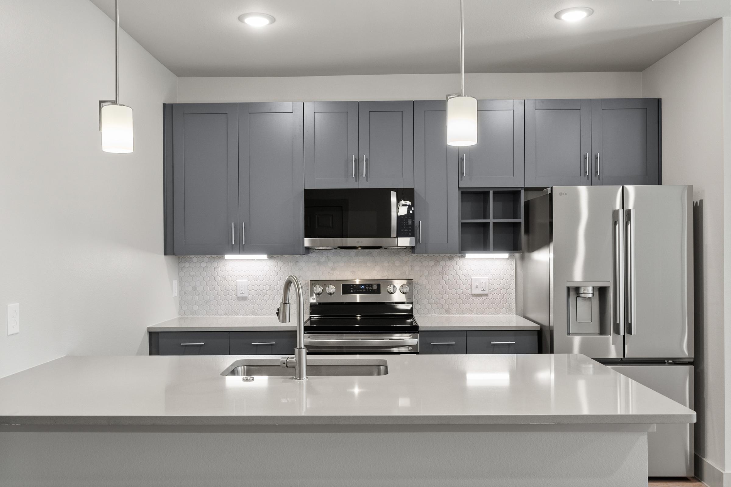 Modern kitchen in the B2 Floor Plan with stainless steel appliances, quartz countertops, pendant lighting, and a large island perfect for cooking and entertaining.