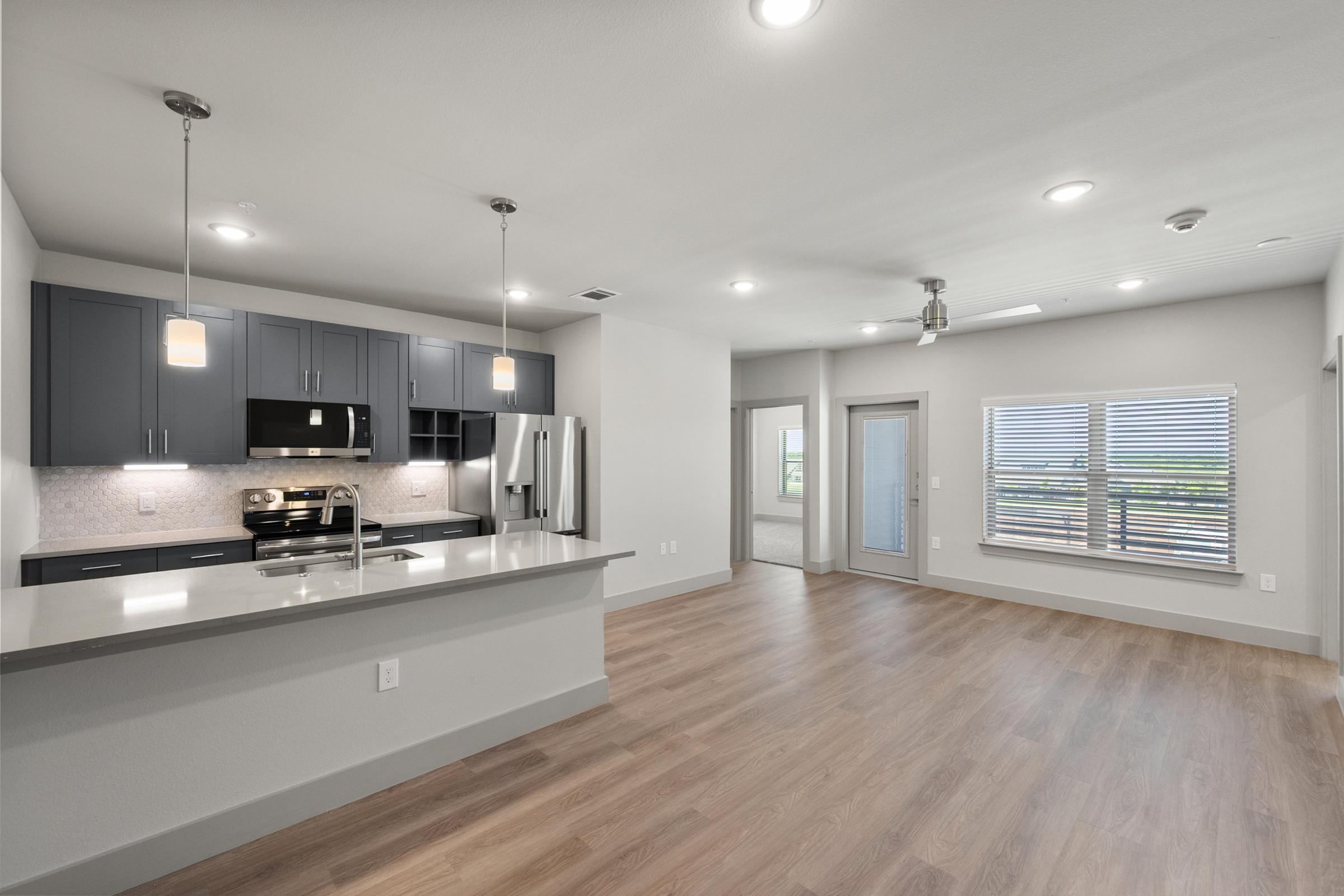Modern kitchen in the B2 Floor Plan with stainless steel appliances, quartz countertops, pendant lighting, and a large island perfect for cooking and entertaining.