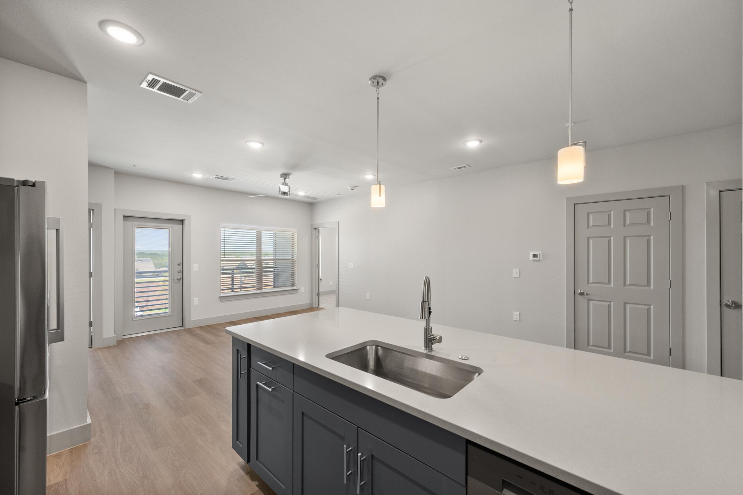 Modern kitchen in the B2 Floor Plan with stainless steel appliances, quartz countertops, pendant lighting, and a large island perfect for cooking and entertaining.