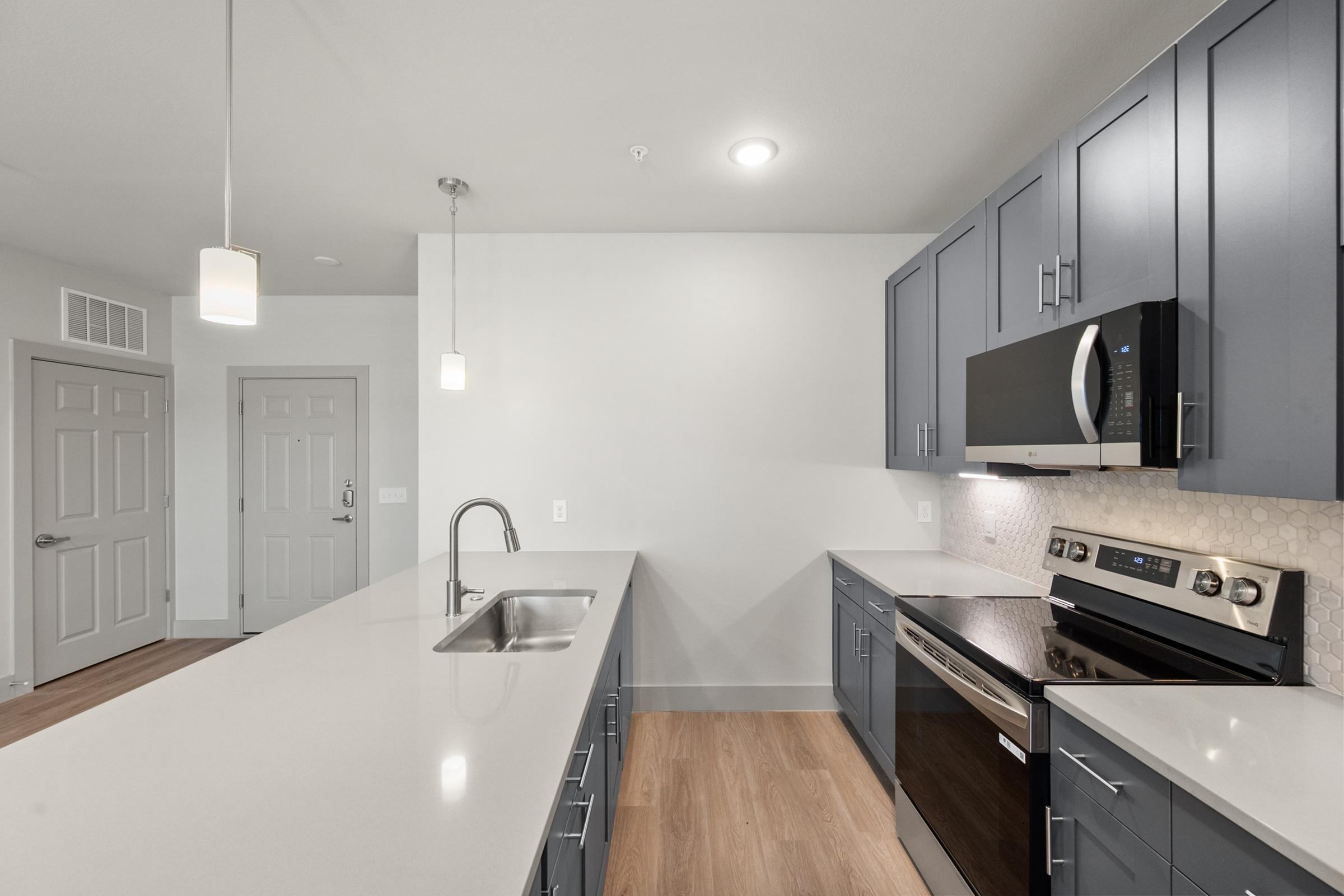 Modern kitchen in the B2 Floor Plan with stainless steel appliances, quartz countertops, pendant lighting, and a large island perfect for cooking and entertaining.