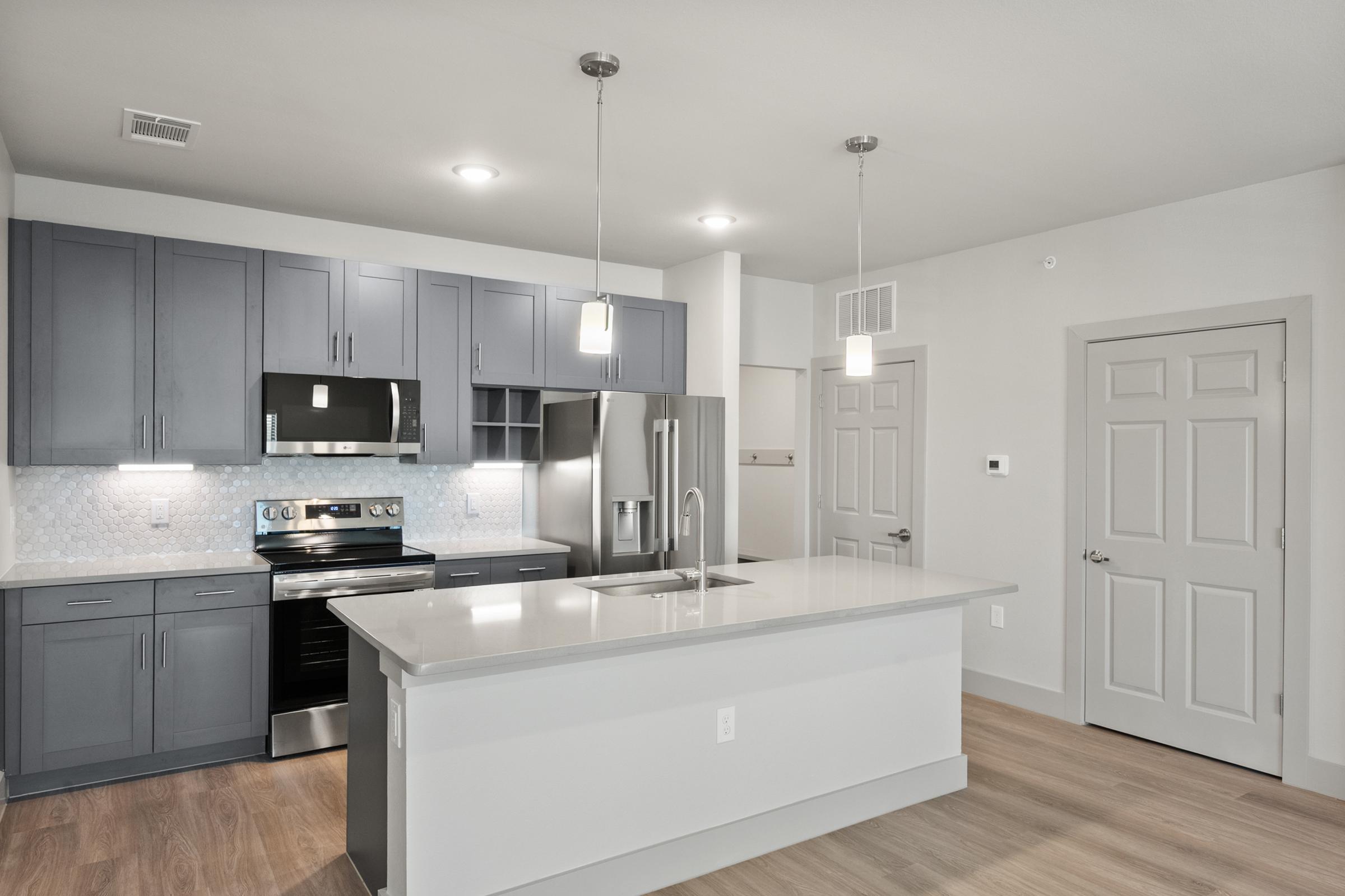Spacious kitchen in the C1 Floor Plan featuring quartz countertops, stainless steel appliances, pendant lighting, soft-close cabinets, a built-in wine rack, and a large center island.