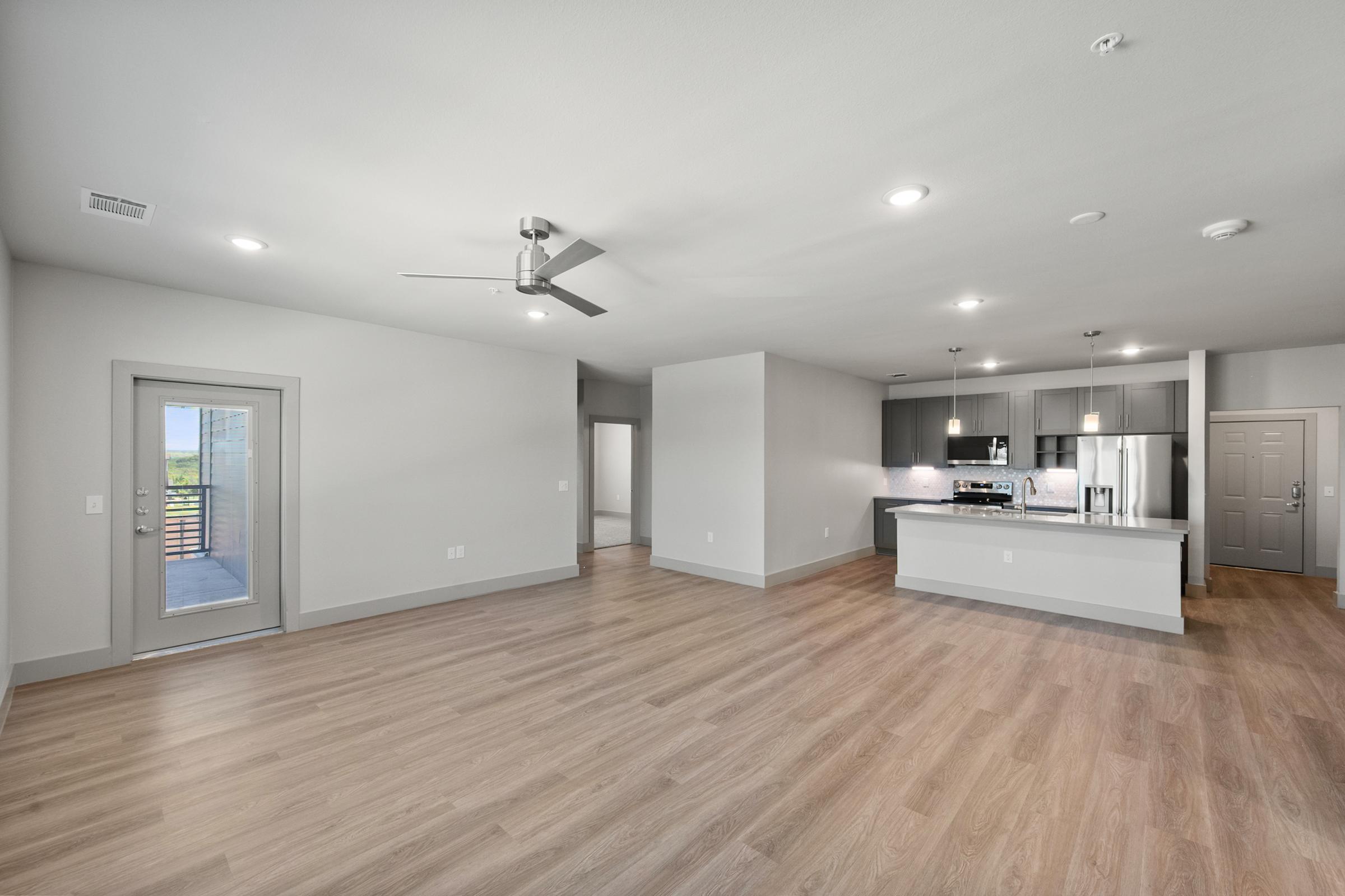 Large open-concept living room in the C1 unit with high ceilings, ceiling fan, and natural light flowing through large windows.