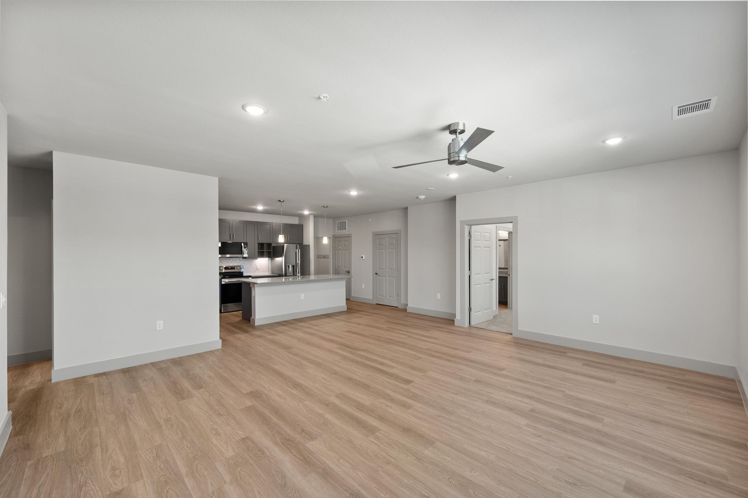 Large open-concept living room in the C1 unit with high ceilings, ceiling fan, and natural light flowing through large windows.