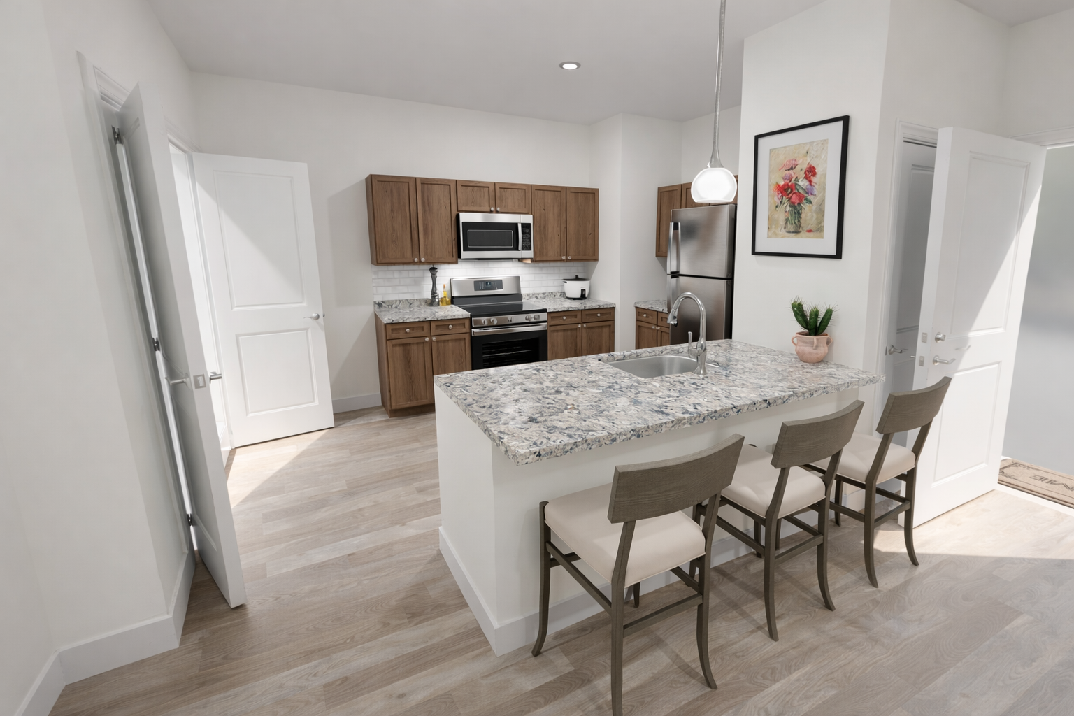 A modern kitchen featuring light wood cabinets, a granite countertop with bar seating for three, stainless steel appliances including a microwave and refrigerator, and a bright, airy atmosphere with light-colored walls and hardwood flooring. A plant and framed artwork add decorative touches.